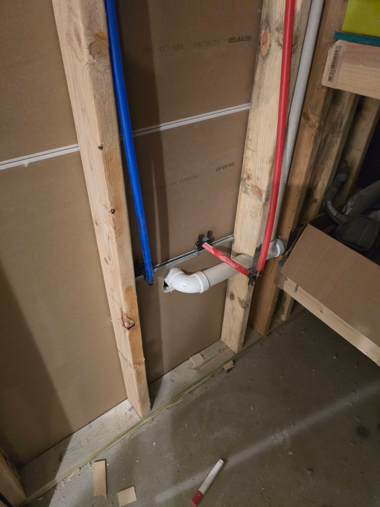 Exposed plumbing in unfinished wall, with blue and red pipes and a white drain fitting.