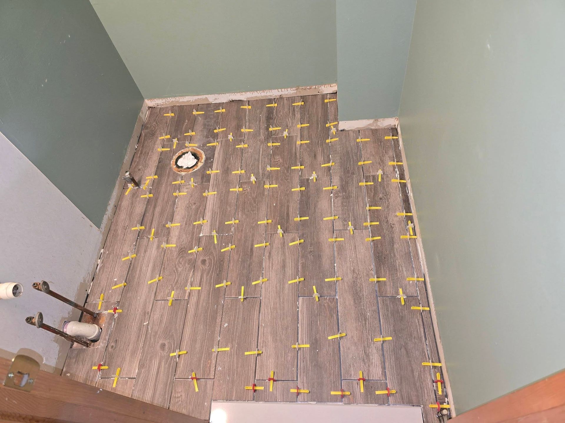 Small tiled bathroom with a shower area, visible toilet flange, and plumbing fixtures along the left wall.