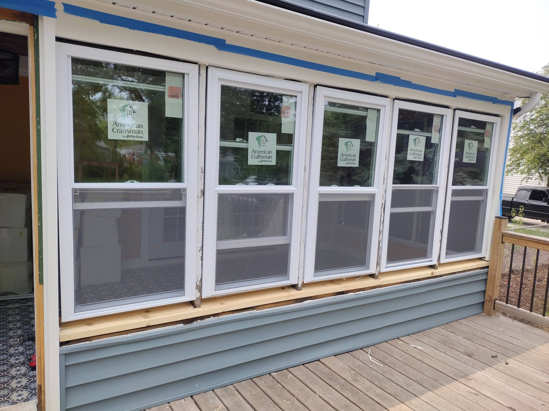 Small house porch with a row of white-framed windows and gray siding under a blue-trimmed roof.