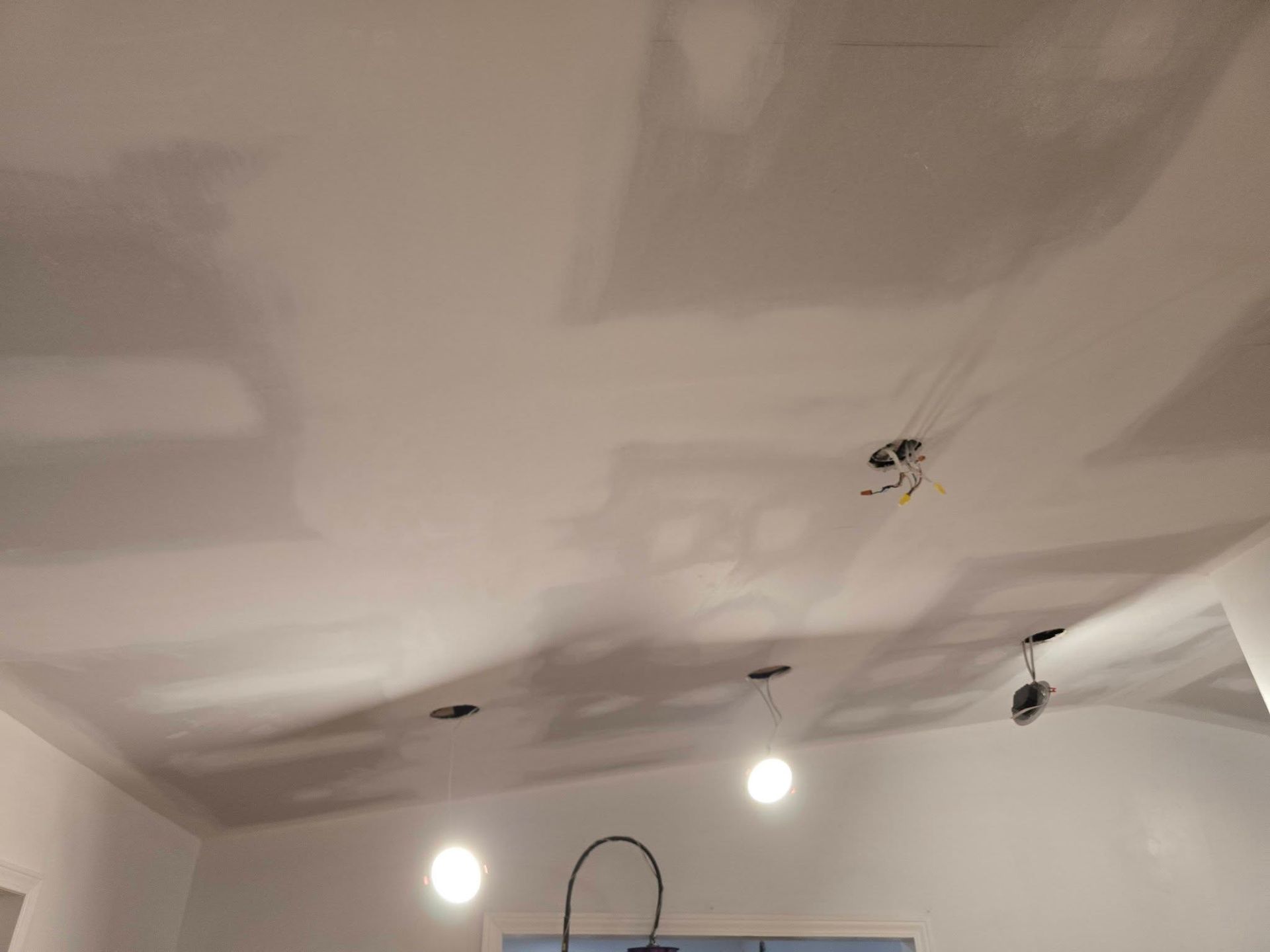 Partially finished white ceiling with drywall patches, recessed lights, and a hanging pendant fixture
