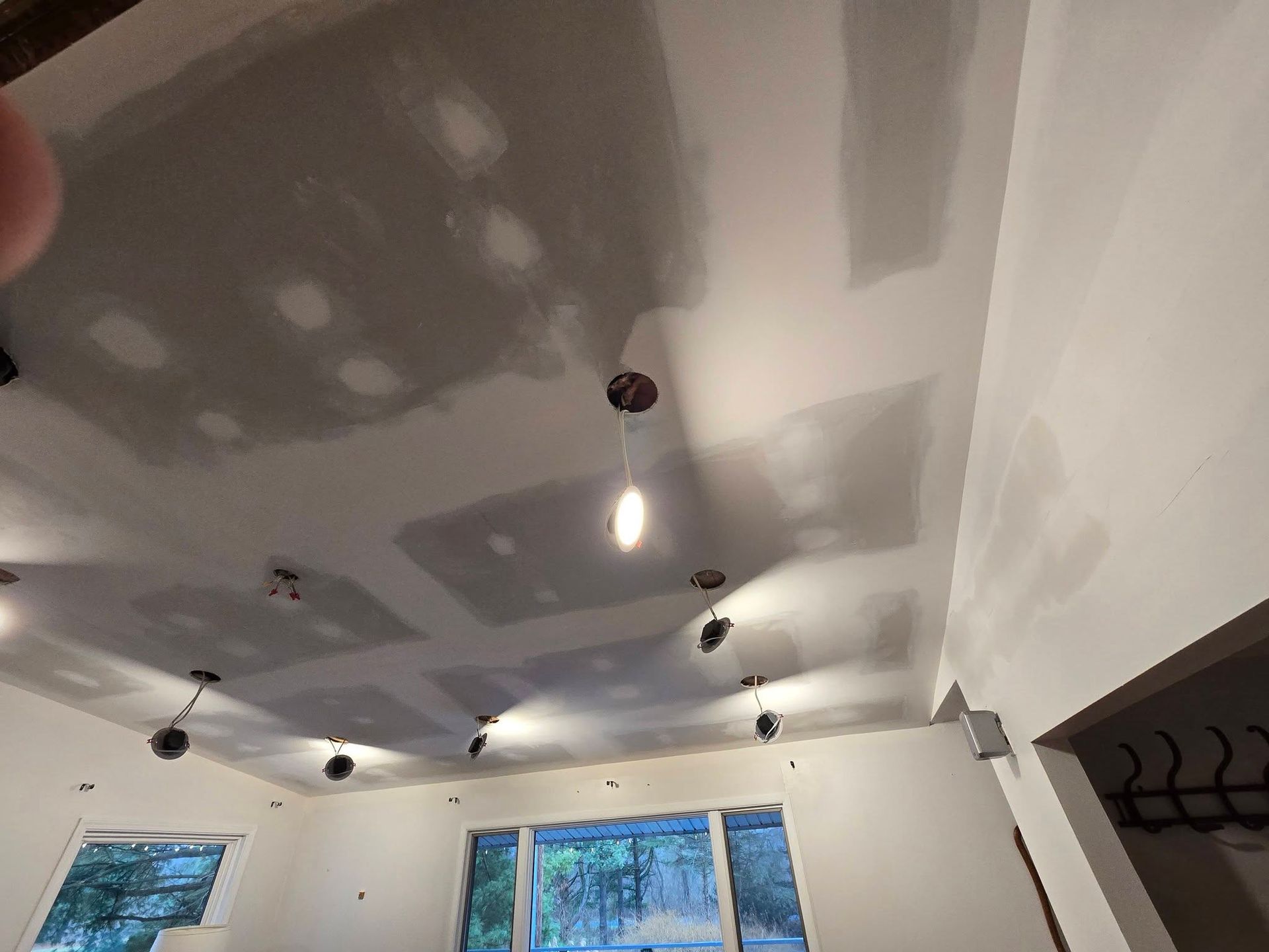 Ceiling under construction with recessed lights, exposed patches, and windows along the wall