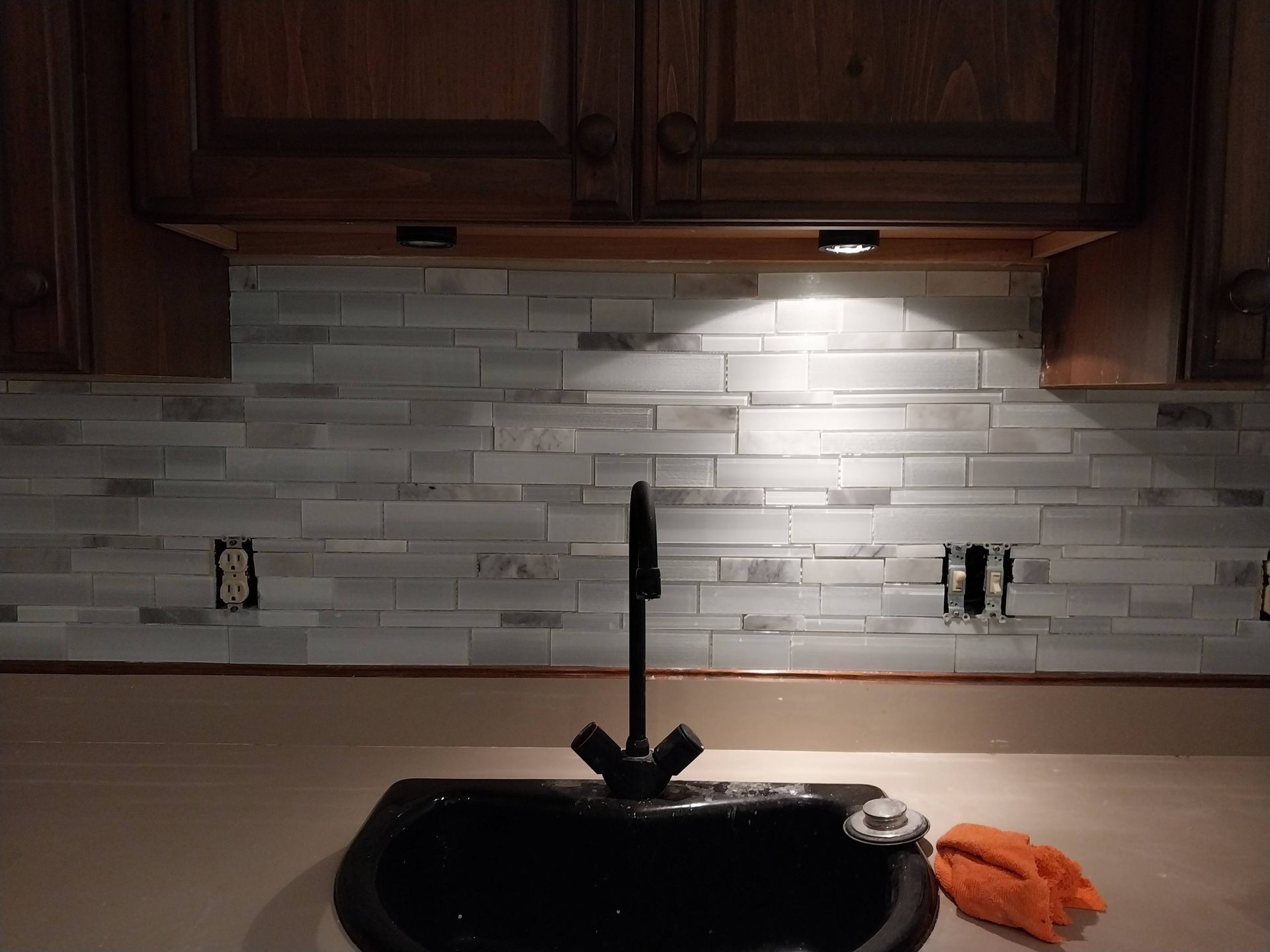 Kitchen sink with dark cabinets, white tile backsplash, and an orange cleaning cloth on the counter
