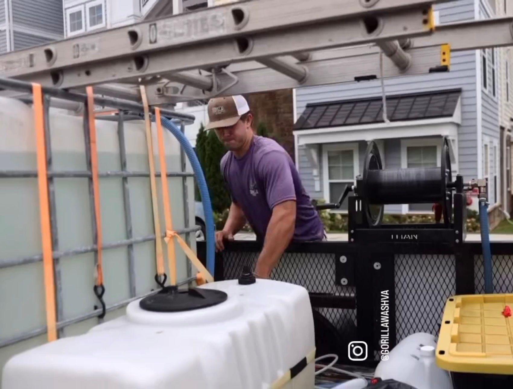 Worker loads a white tank onto a truck using a ladder and straps in a driveway