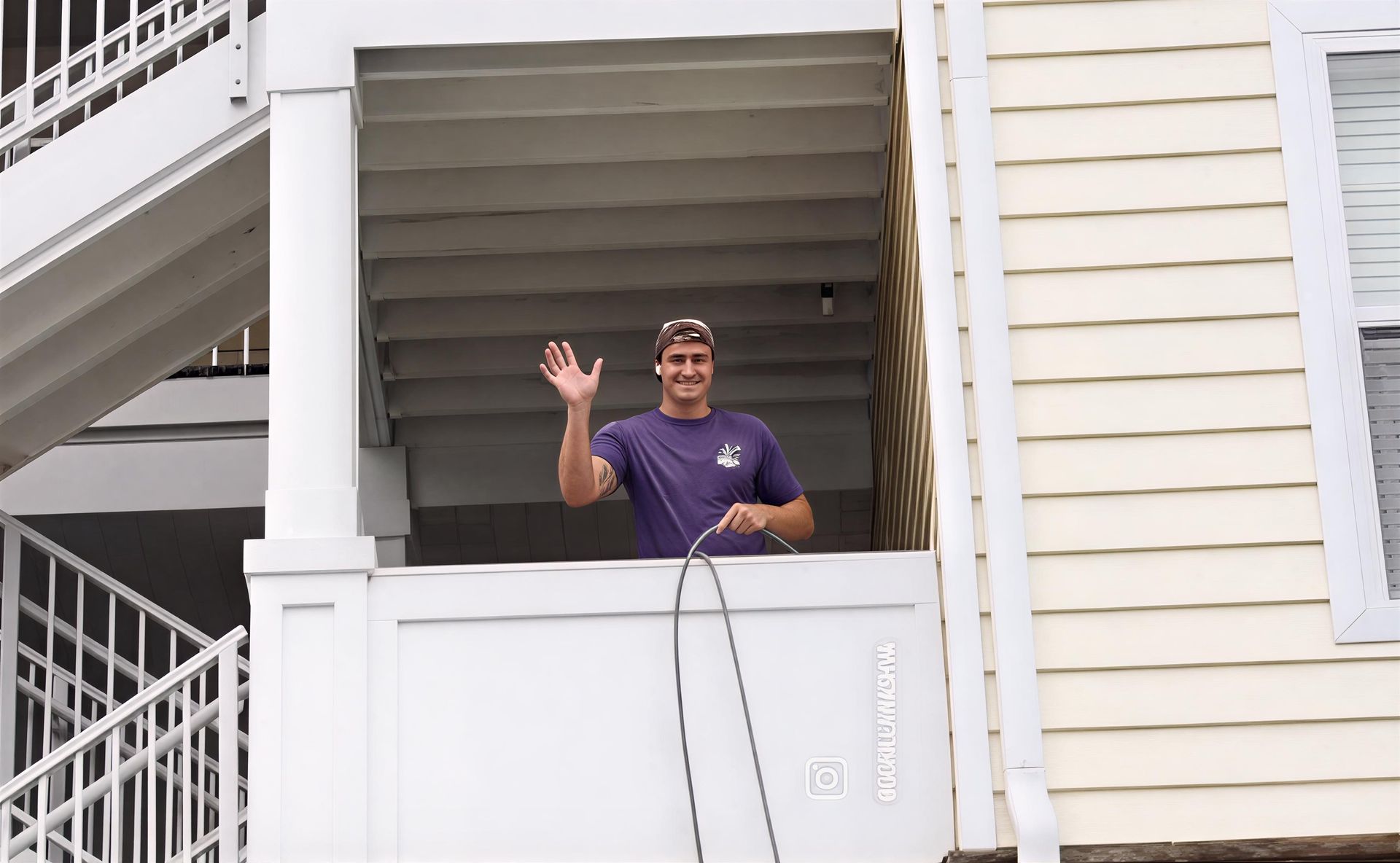 Person in purple shirt waving from a white balcony beside stairs and siding.