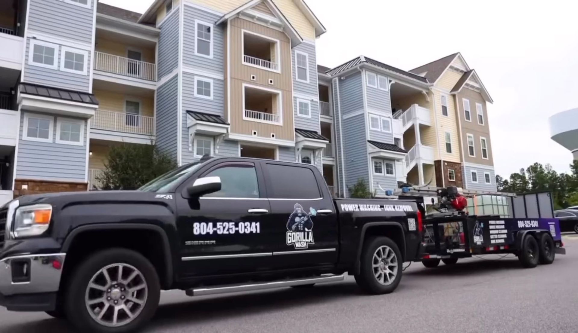 Black tow truck with trailer parked by apartment buildings in a residential street.