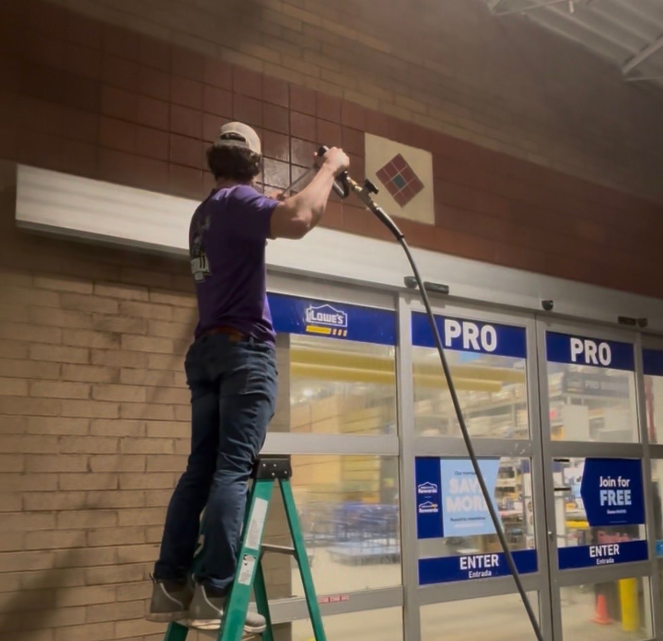Worker on a ladder installing a sign above a store entrance at night