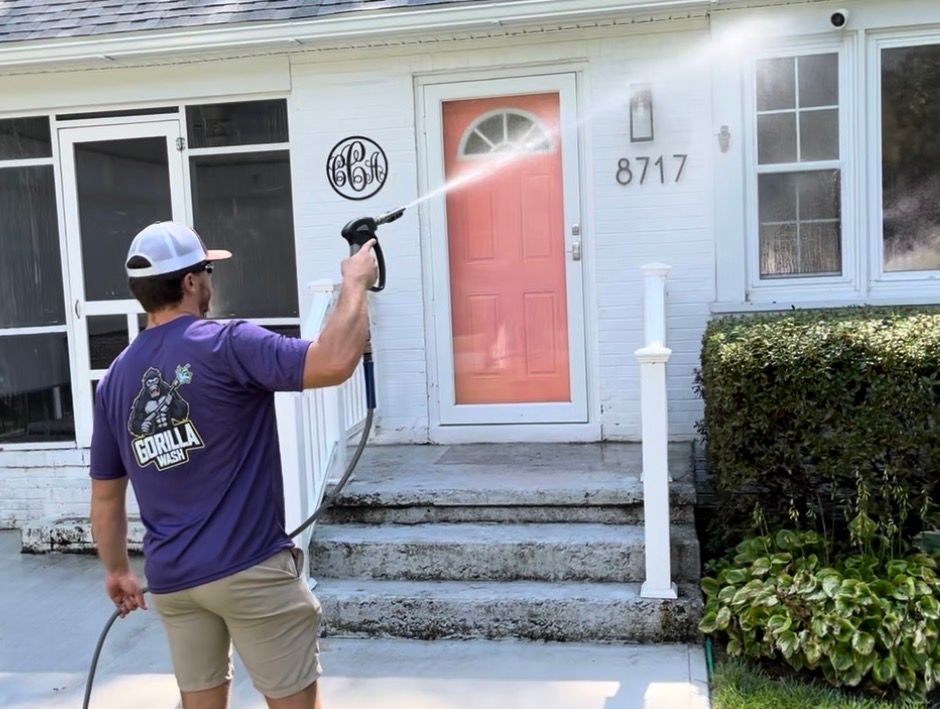 Worker pressure-washing the front of a white house with a red door and porch steps
