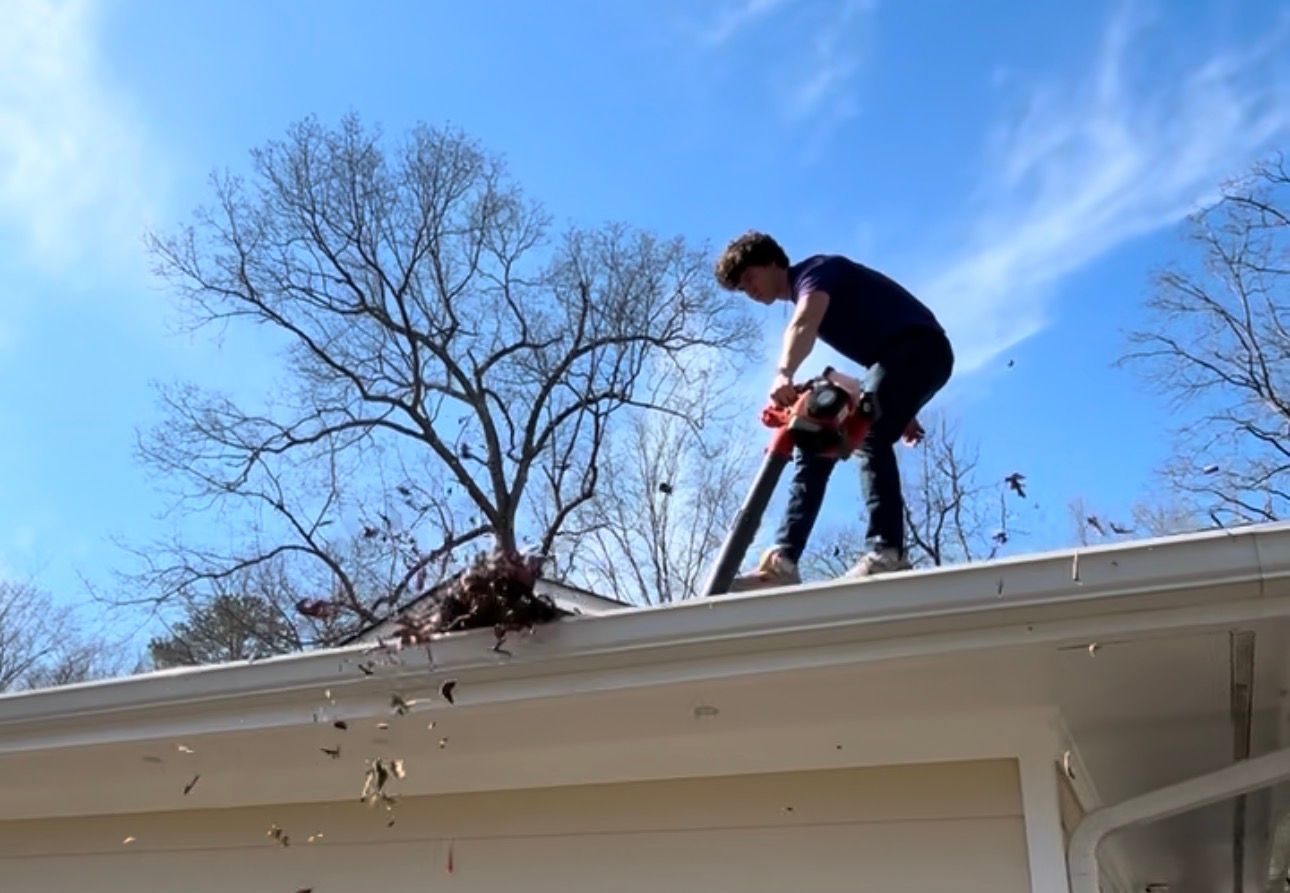 Person using a chainsaw on a roof near bare trees under a blue sky