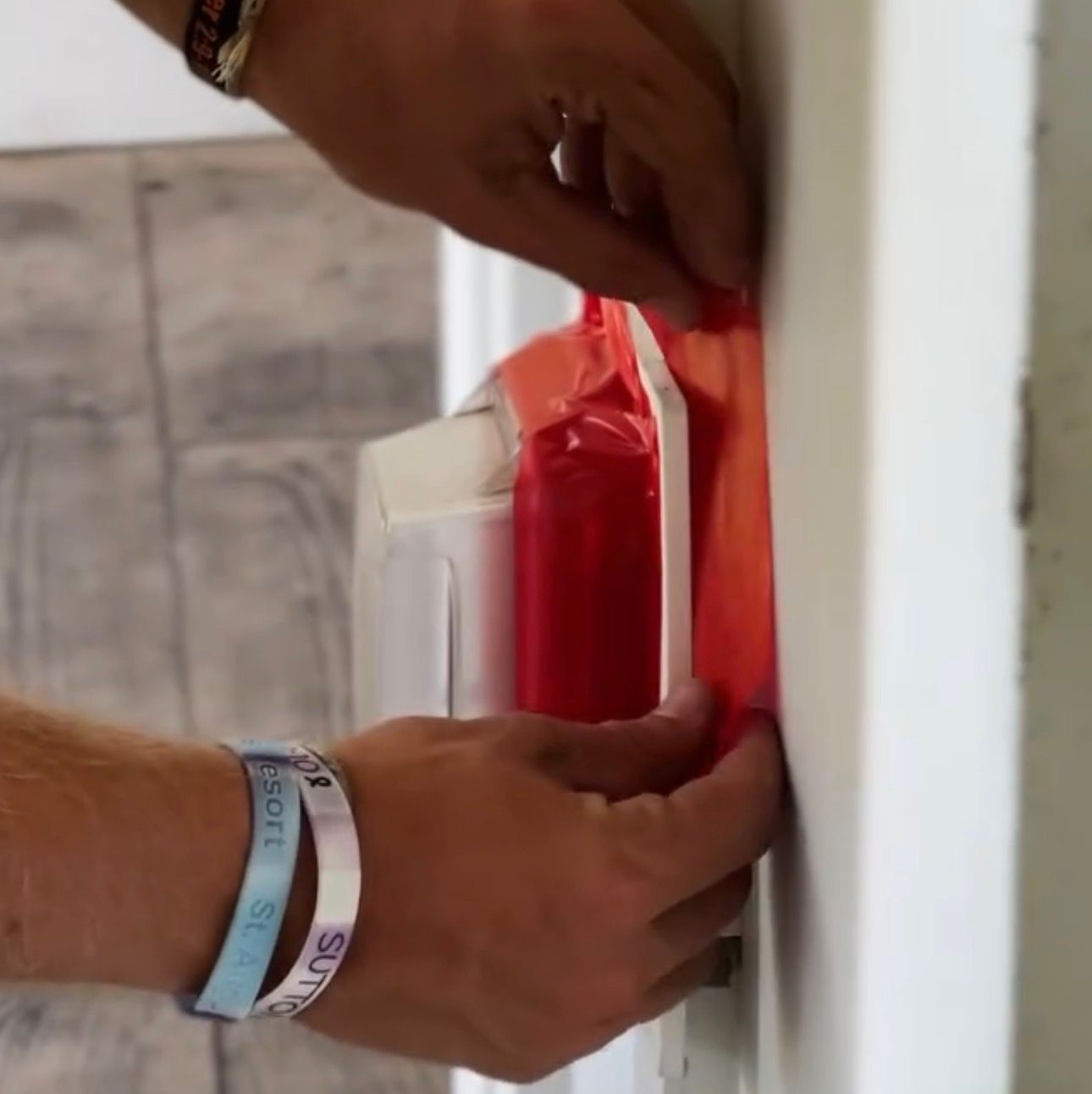 Hands peeling red protective film from a white appliance beside a door frame.