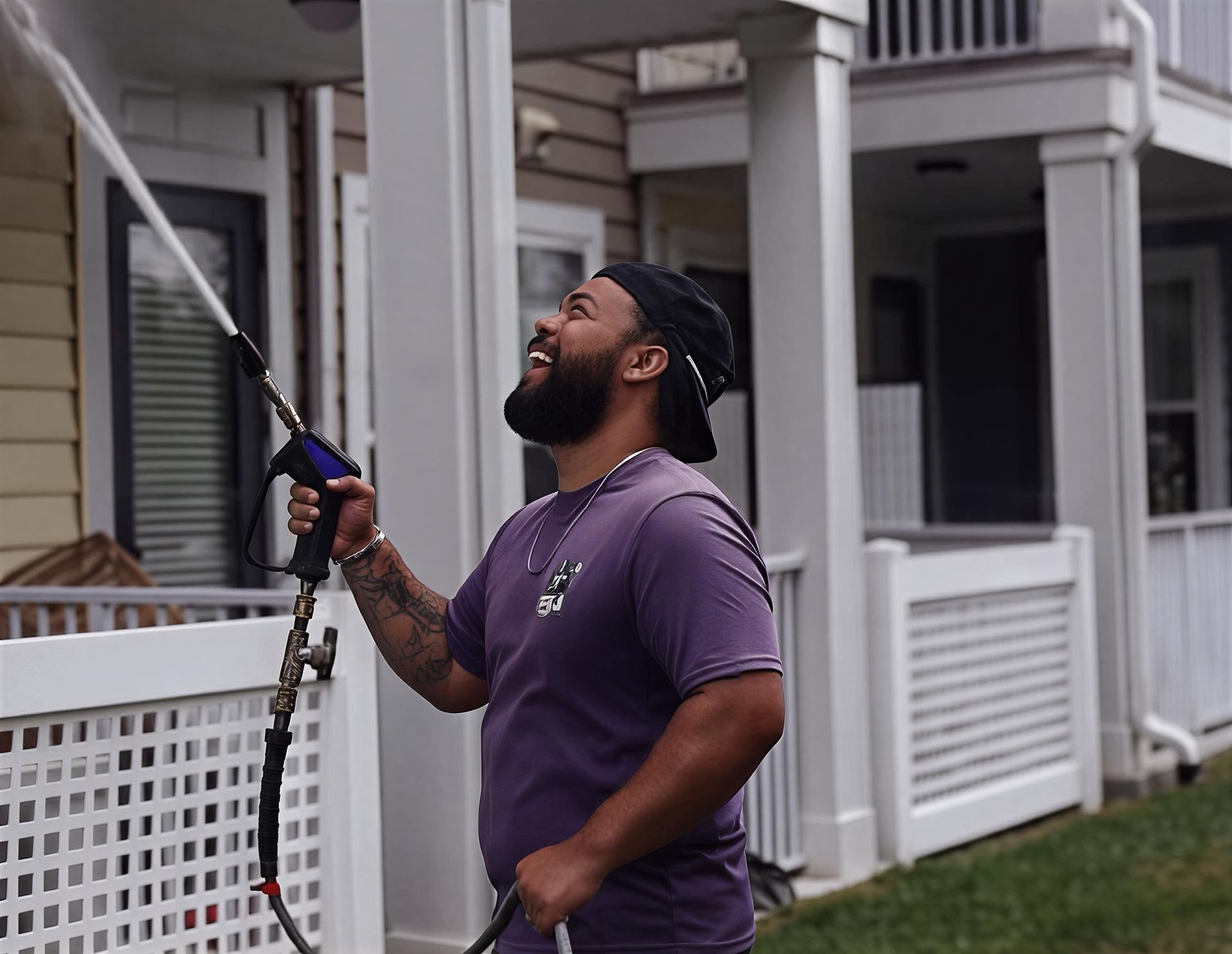 Man using a pressure washer to clean a white porch railing at a house