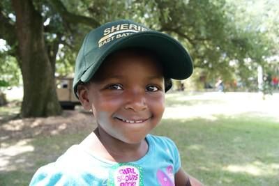 Girl in a green hat and blue shirt smiles in a park.