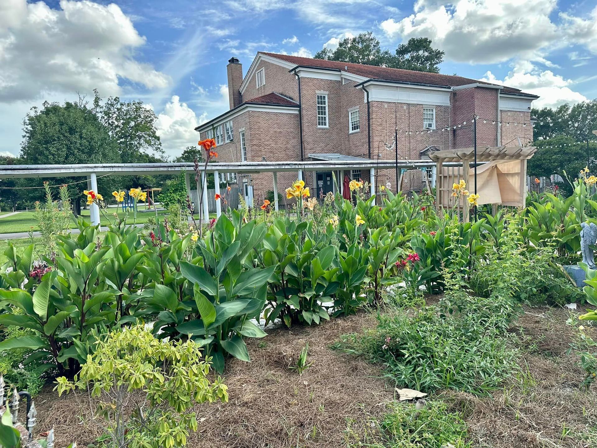 A brick building with a garden in front. Yellow and red flowers are blooming under a cloudy sky.