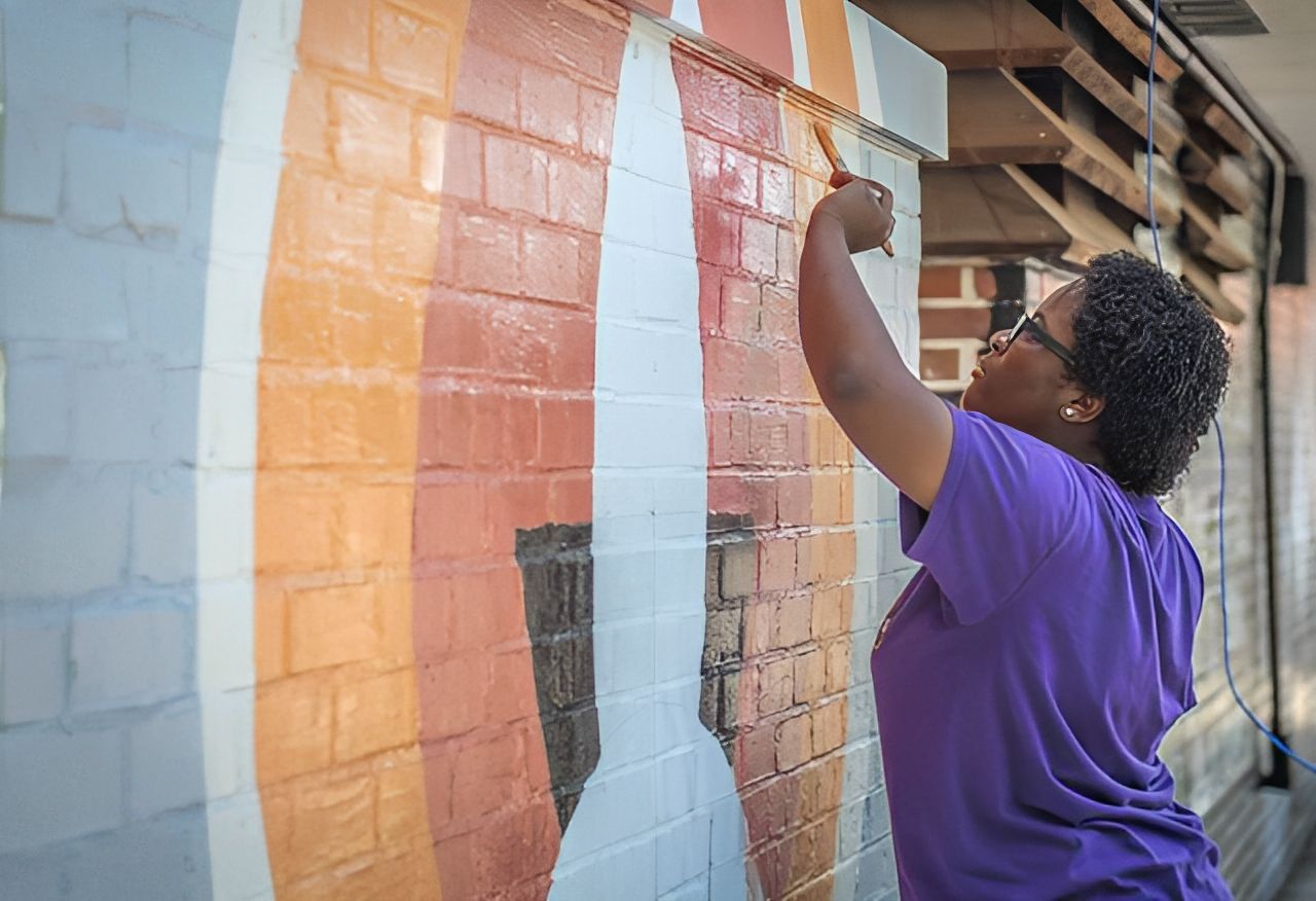 Woman painting a colorful mural on a brick wall with a paintbrush.