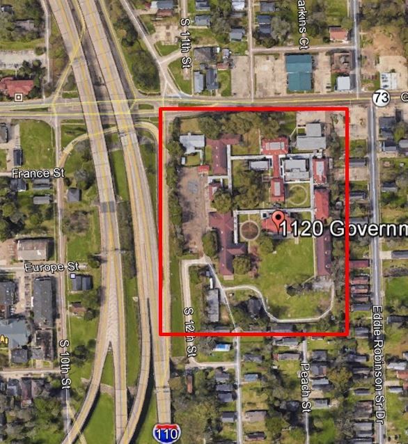 Aerial view of 1120 Government St. in Baton Rouge, Louisiana; a complex of buildings surrounded by trees and a red boundary.