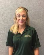 Woman with blonde hair wearing a green polo shirt smiling in front of a gray wall.