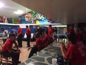 People in red shirts in a room with a bar, some seated, some standing. Graffiti art on the wall.