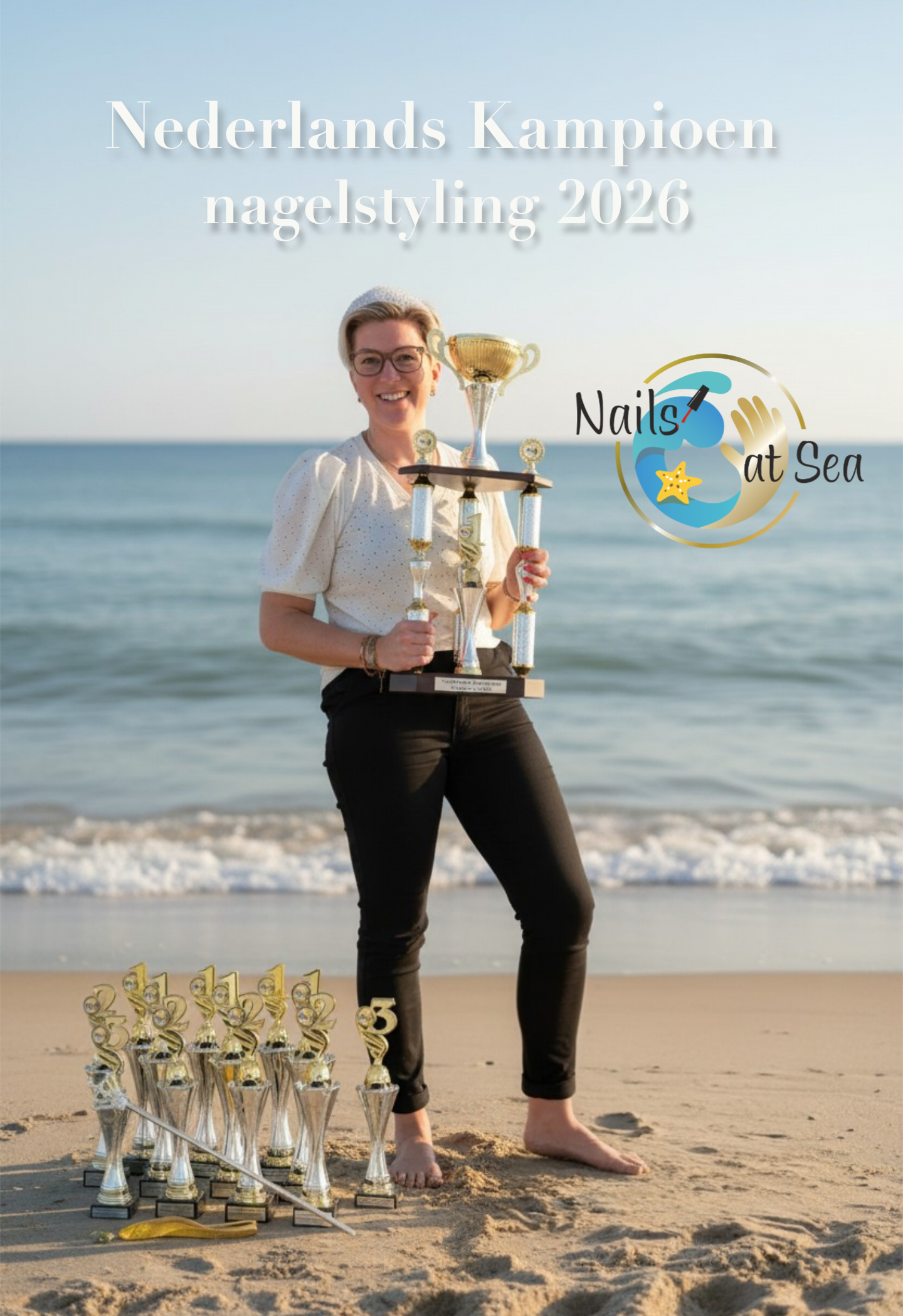 Een nagelstyliste houdt een grote trofee vast op een strand, omringd door verschillende kleinere trofeeën met de tekst 