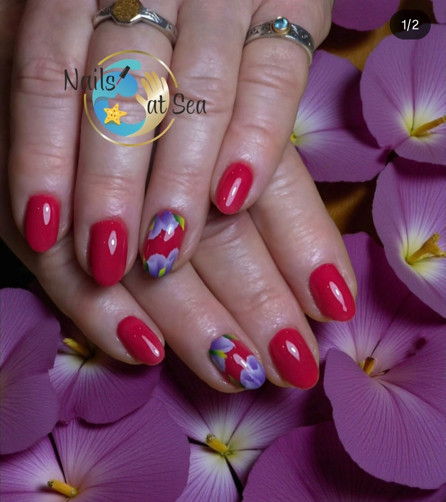 Handen met rood gemanicuurde nagels met bloemaccenten, rustend op een achtergrond van paarse bloemen.