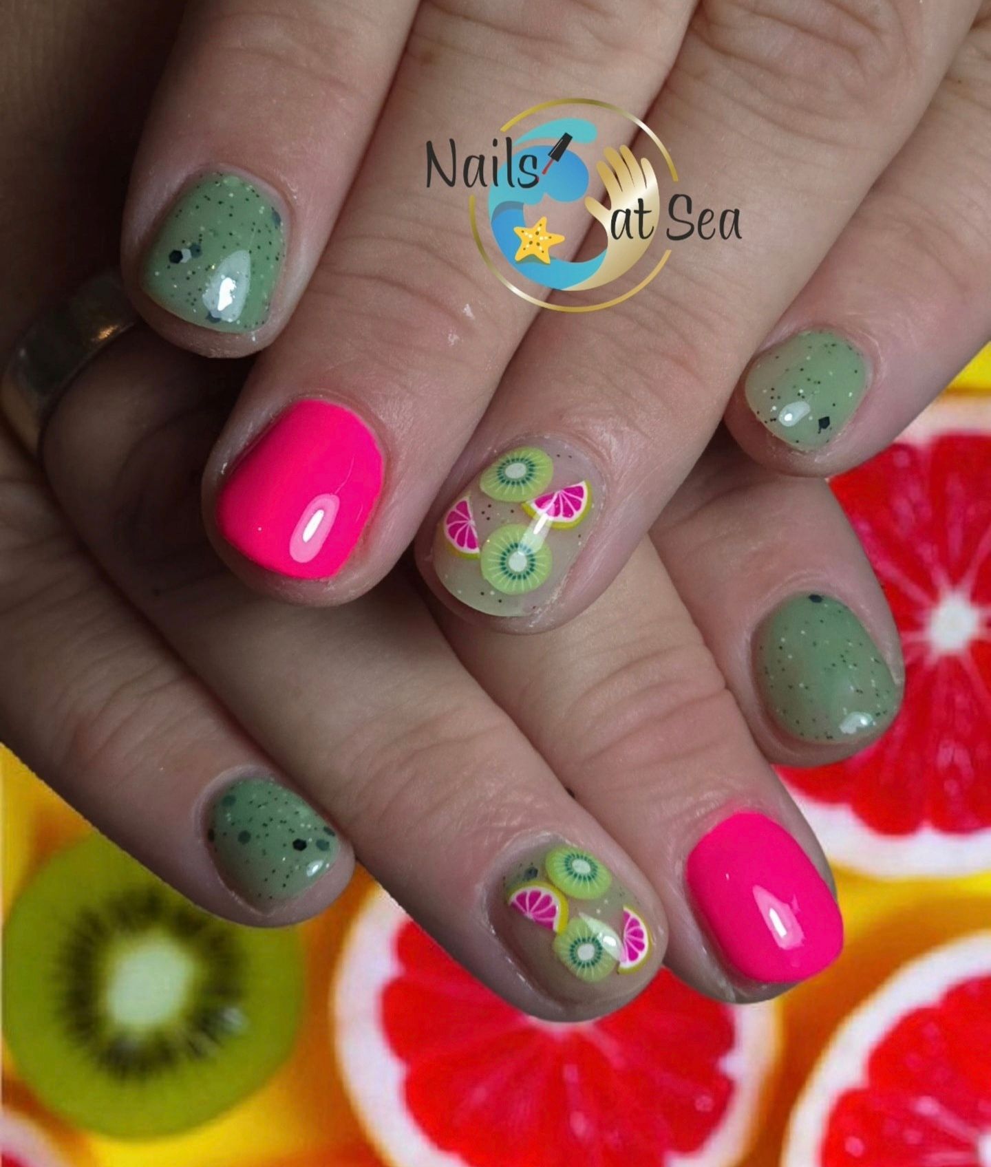 Verzorgde nagels met felroze nagellak, saliegroene spikkels en kleine accenten van kiwi- en citrusvruchtschijfjes.