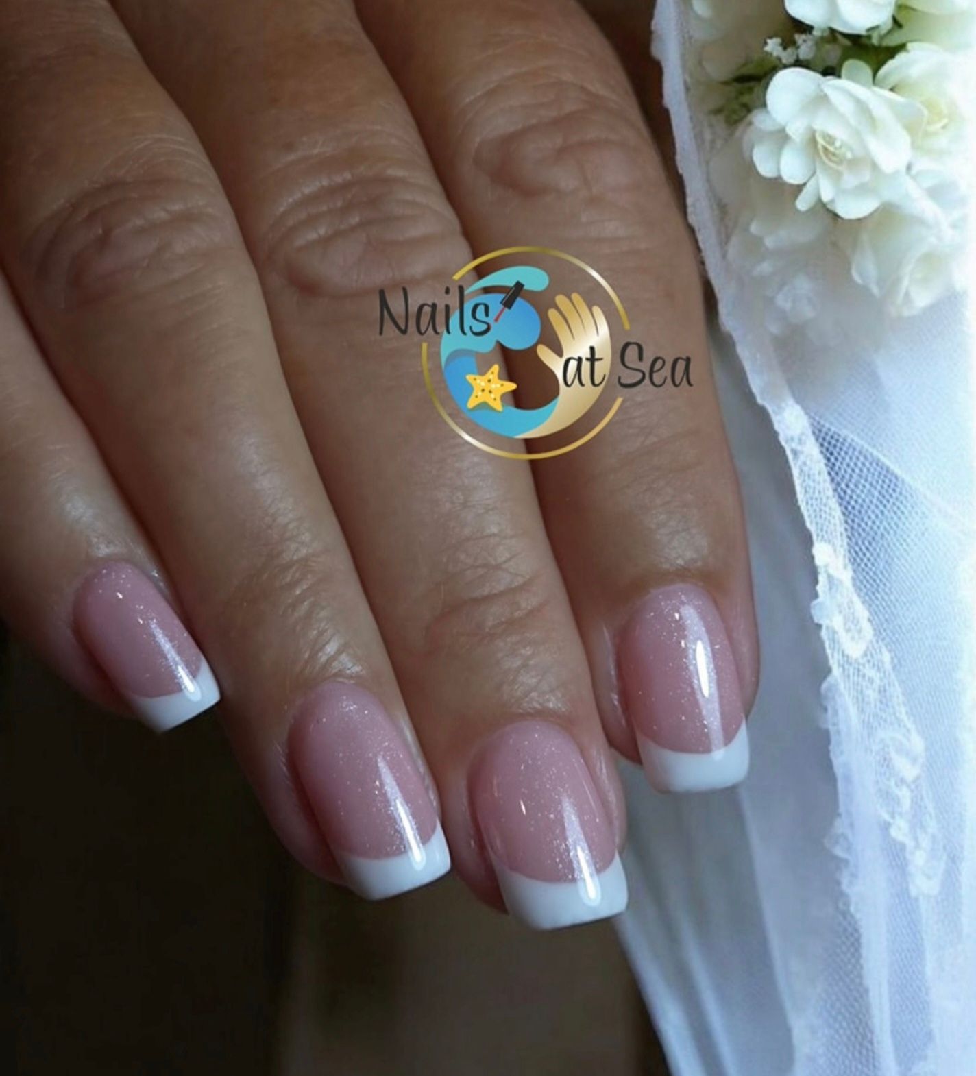 Een close-up van een hand met een klassieke Franse manicure, met roze nagels met witte uiteinden, tegen een witte achtergrond.