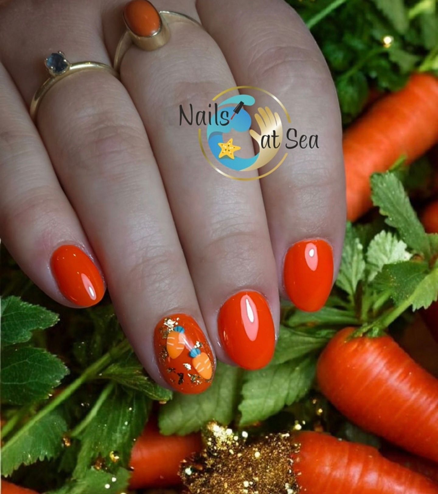 Een hand met feloranje nagellak op alle nagels, waarvan één een klein worteltje als ontwerp heeft, rustend op een bedje van verse wortels.