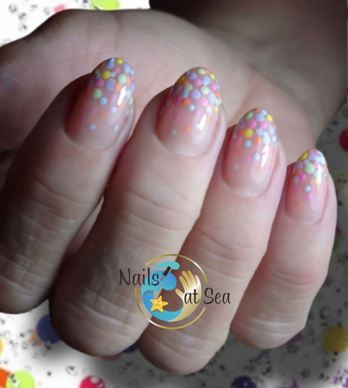 Nagels met een transparante basis en een kleurrijk pastelkleurig stippenpatroon op de uiteinden.