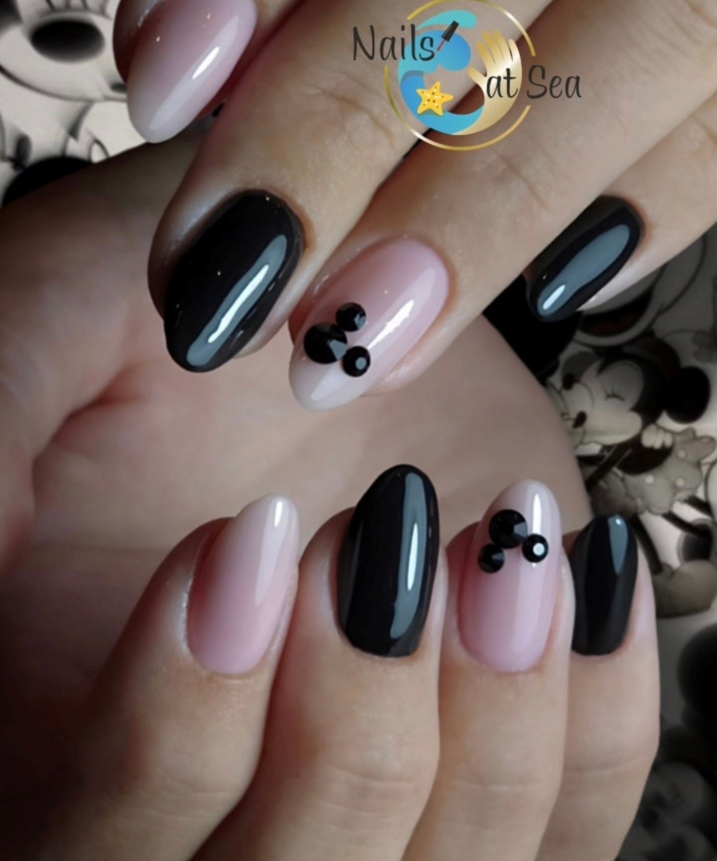 Verzorgde nagels met afwisselend lichtroze en glanzend zwarte nagellak, versierd met kleine zwarte Mickey Mouse-pictogrammen.
