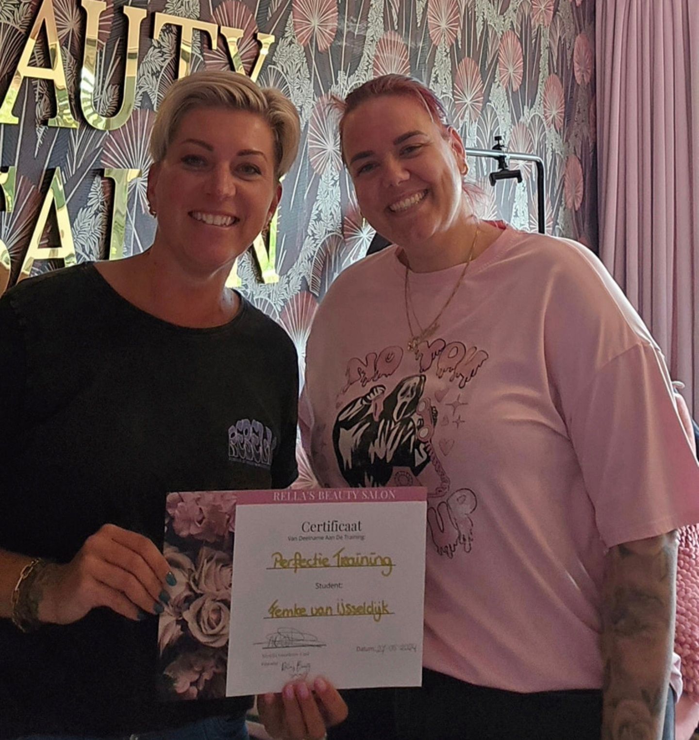 Twee personen staan ​​lachend in een salon en houden een certificaat voor 