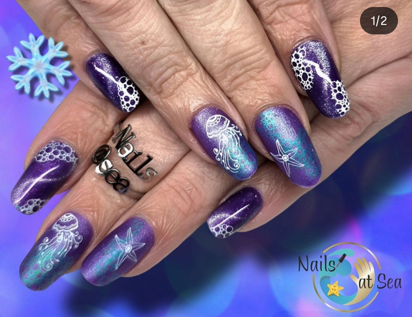 Verzorgde vingernagels met een paars-blauwe kleurovergang, geaccentueerd door witte stempels van kwallen en zeesterren.