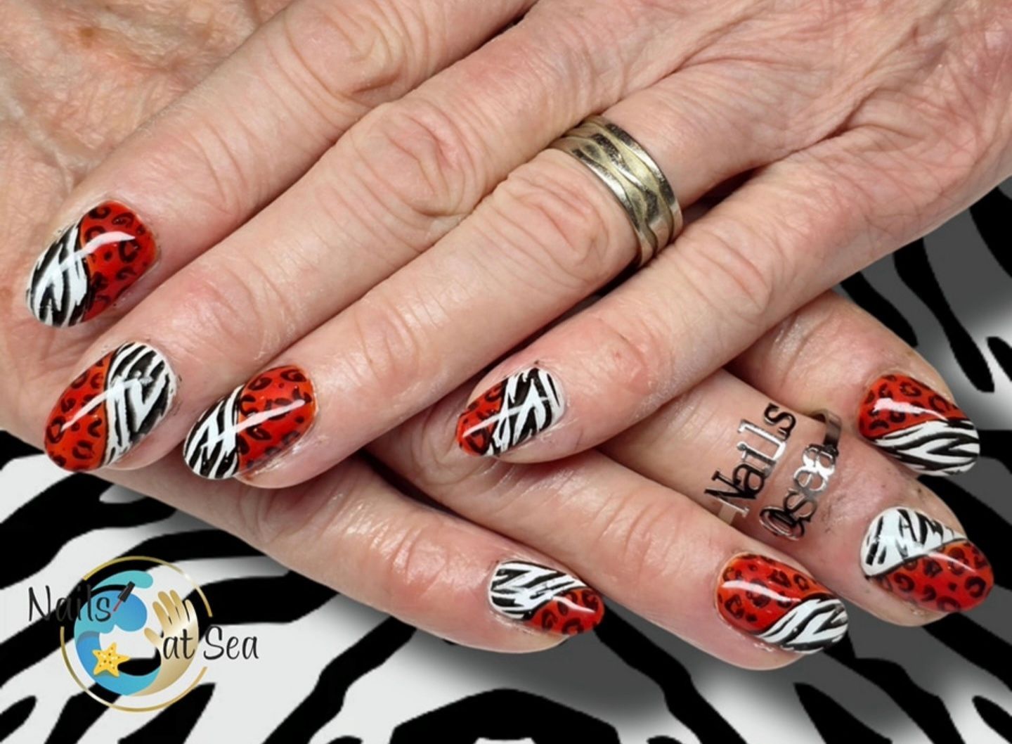 Een close-up van handen met gemanicuurde nagels, versierd met een rode luipaardprint en een wit-zwart zebrapatroon.