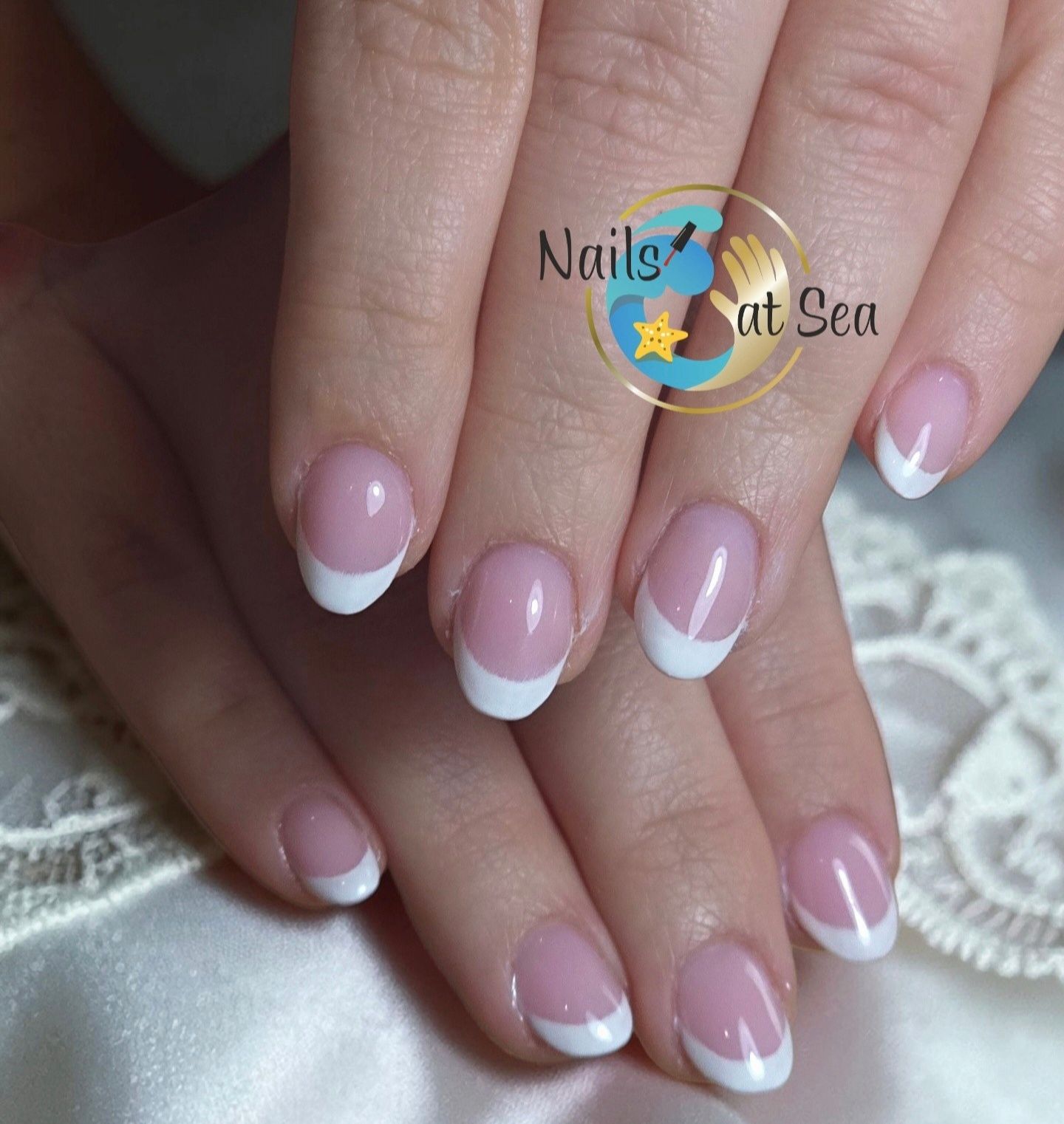 Een paar handen met verzorgde, korte ovale nagels, voorzien van een klassieke roze-witte Franse manicure.