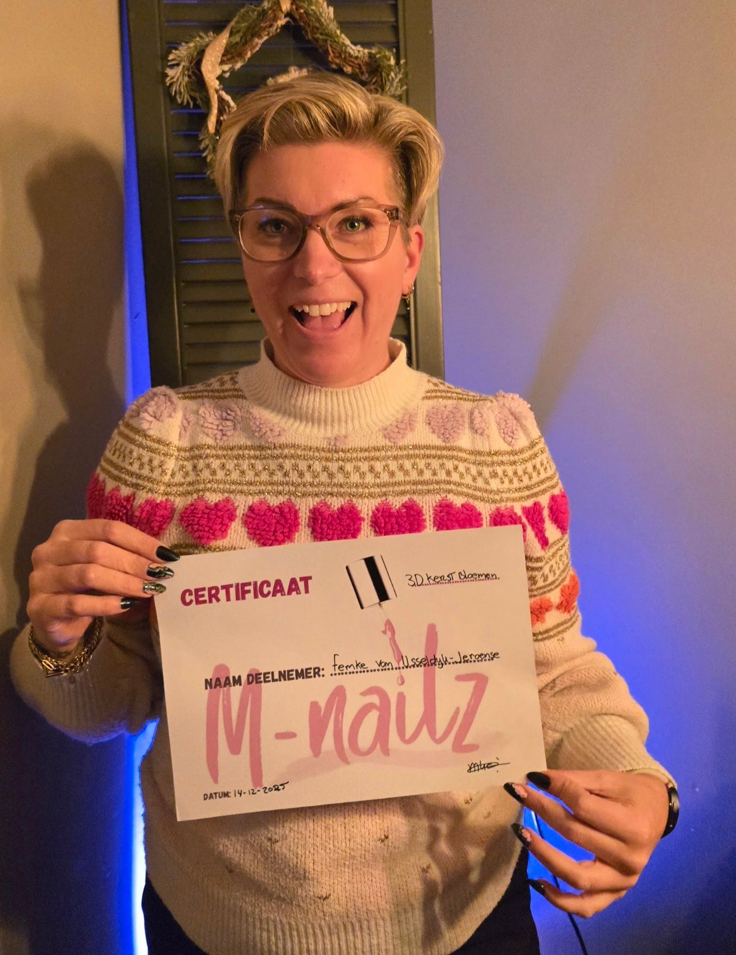 Een persoon, gekleed in een trui met roze hartjes, lacht terwijl hij een certificaat van 