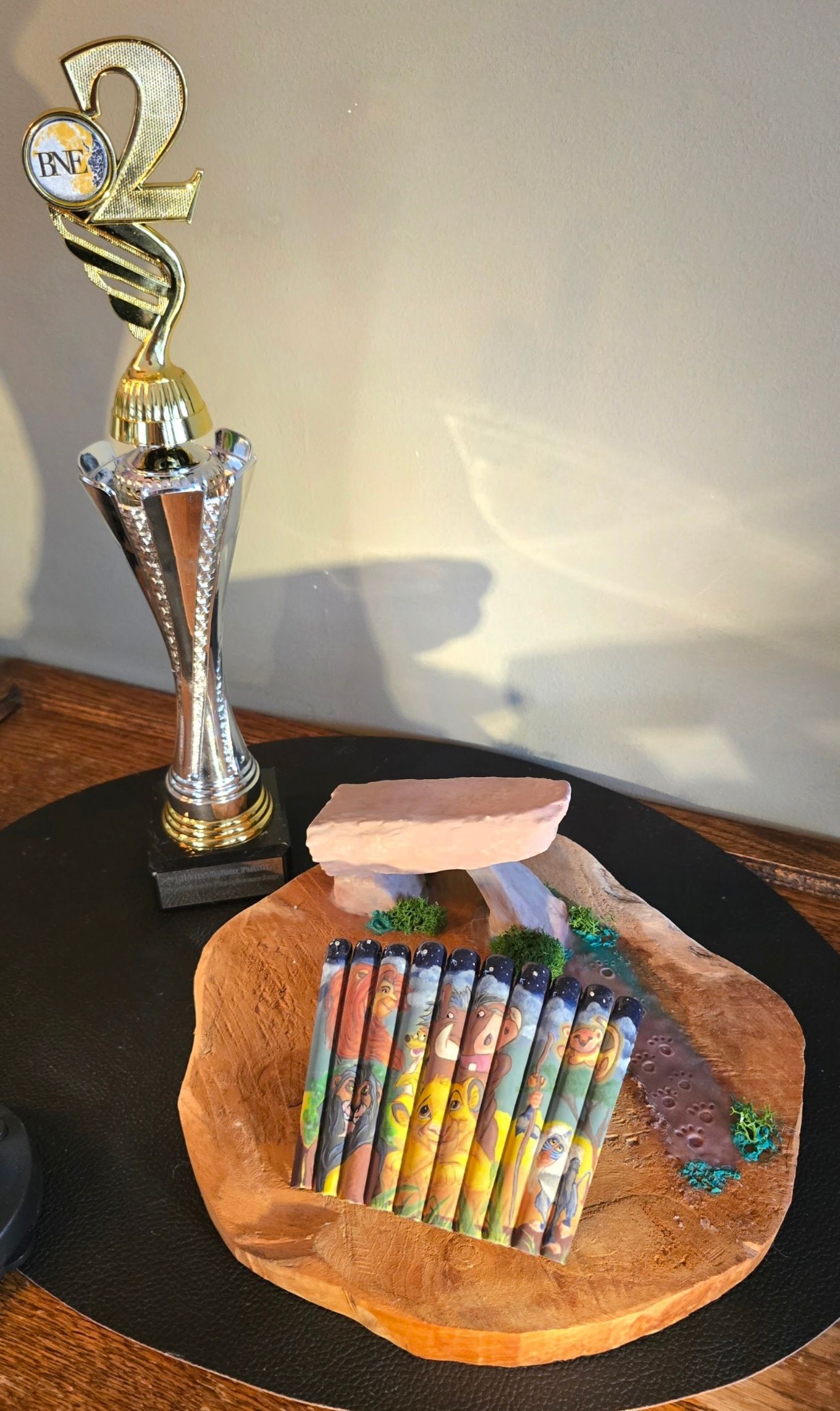 Een goudkleurige trofee staat naast een model van een stenen constructie met kleurrijke stokjes op een ronde, gestructureerde voet.