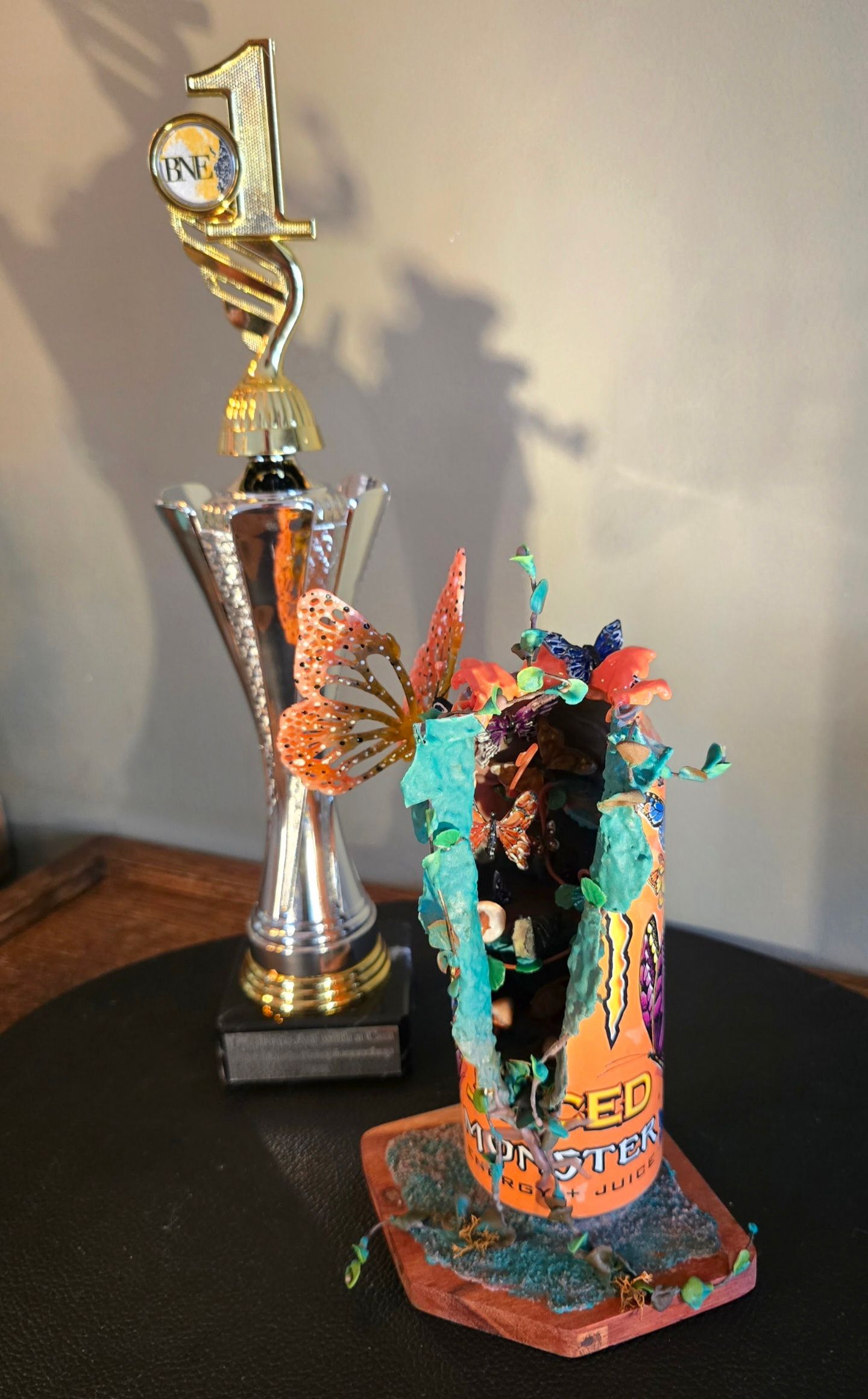 Naast een versierd, hergebruikt blikje sinaasappelsoda staat een trofee voor de eerste plaats, met een uitgesneden figuurtje, een vlinder en kralen.