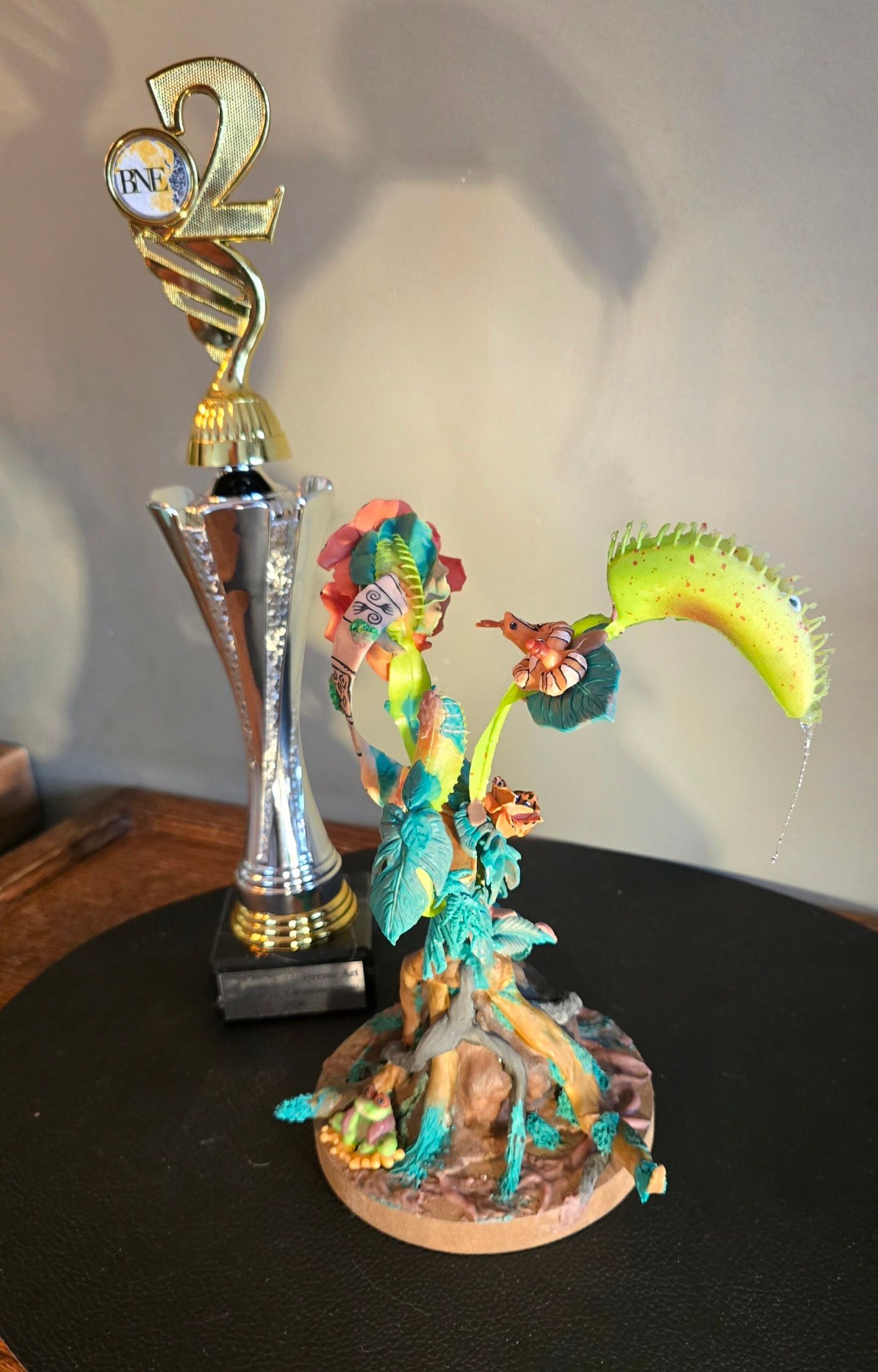 Naast een gedetailleerd, kleurrijk model van een venusvliegenvanger met meerdere groene vallen staat een gouden trofee.