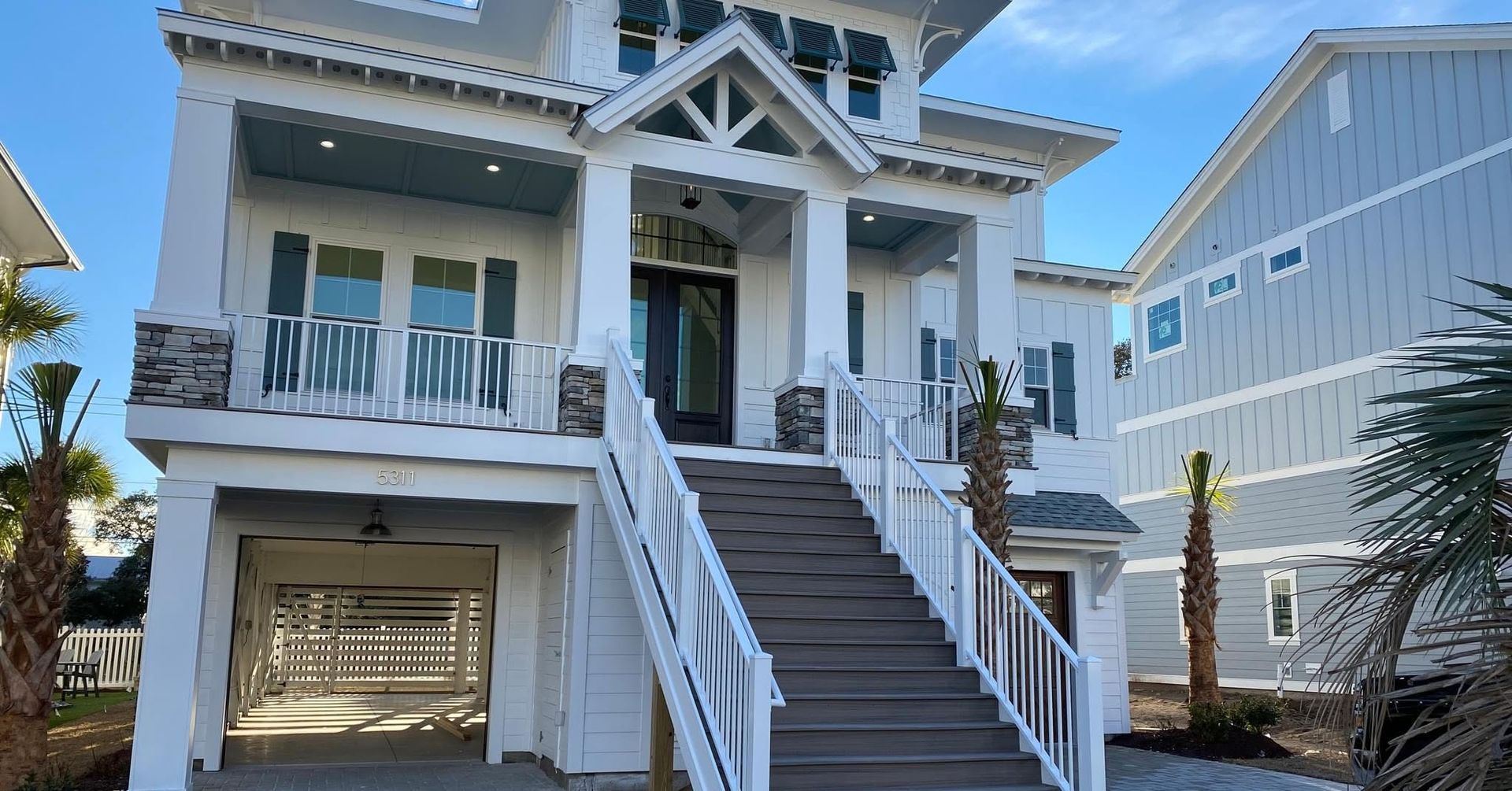 White beach house with front stairs, balcony, and garage under a bright blue sky