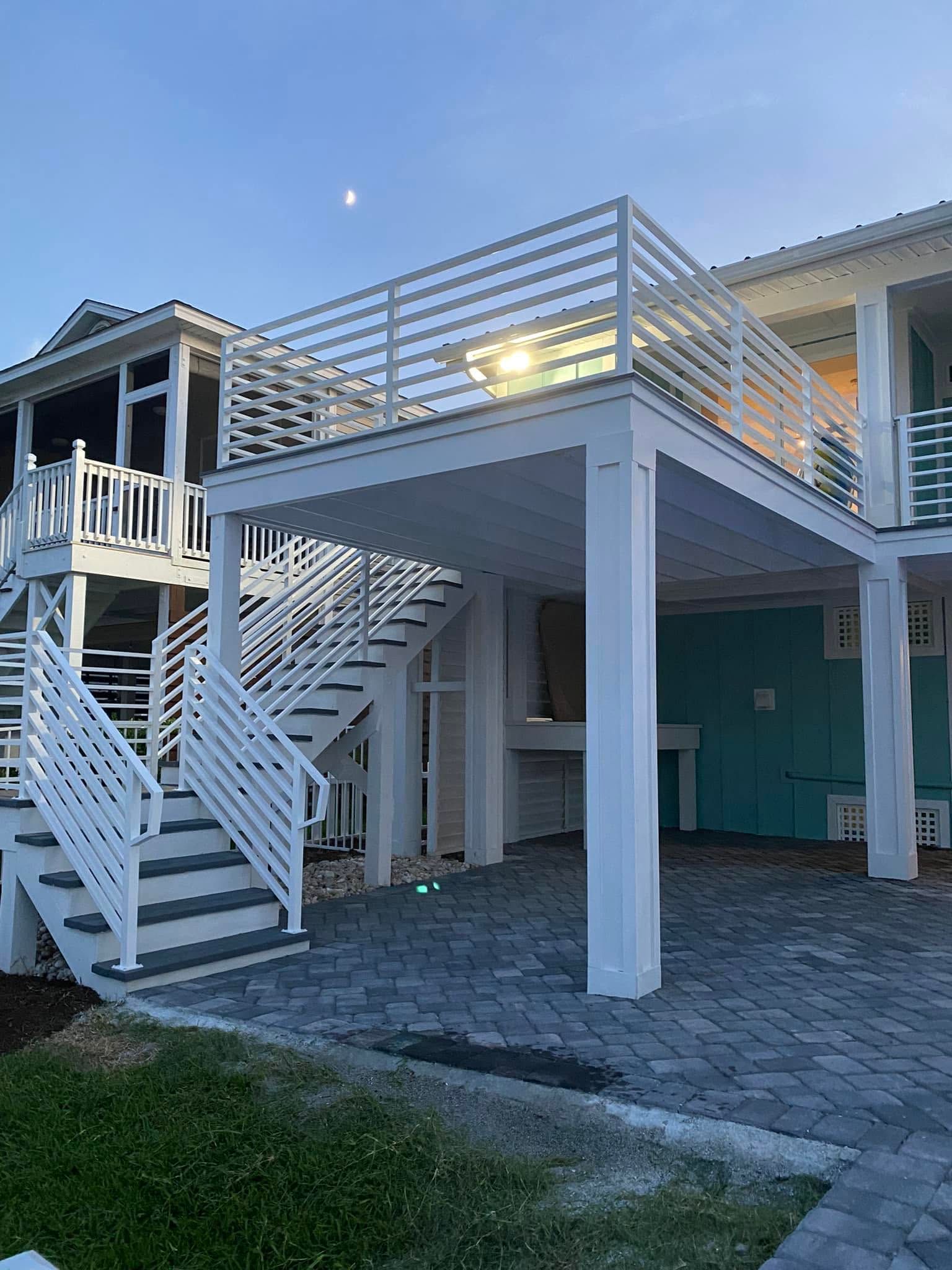 Exterior of a raised white building with stairs, balcony, and paved courtyard at dusk