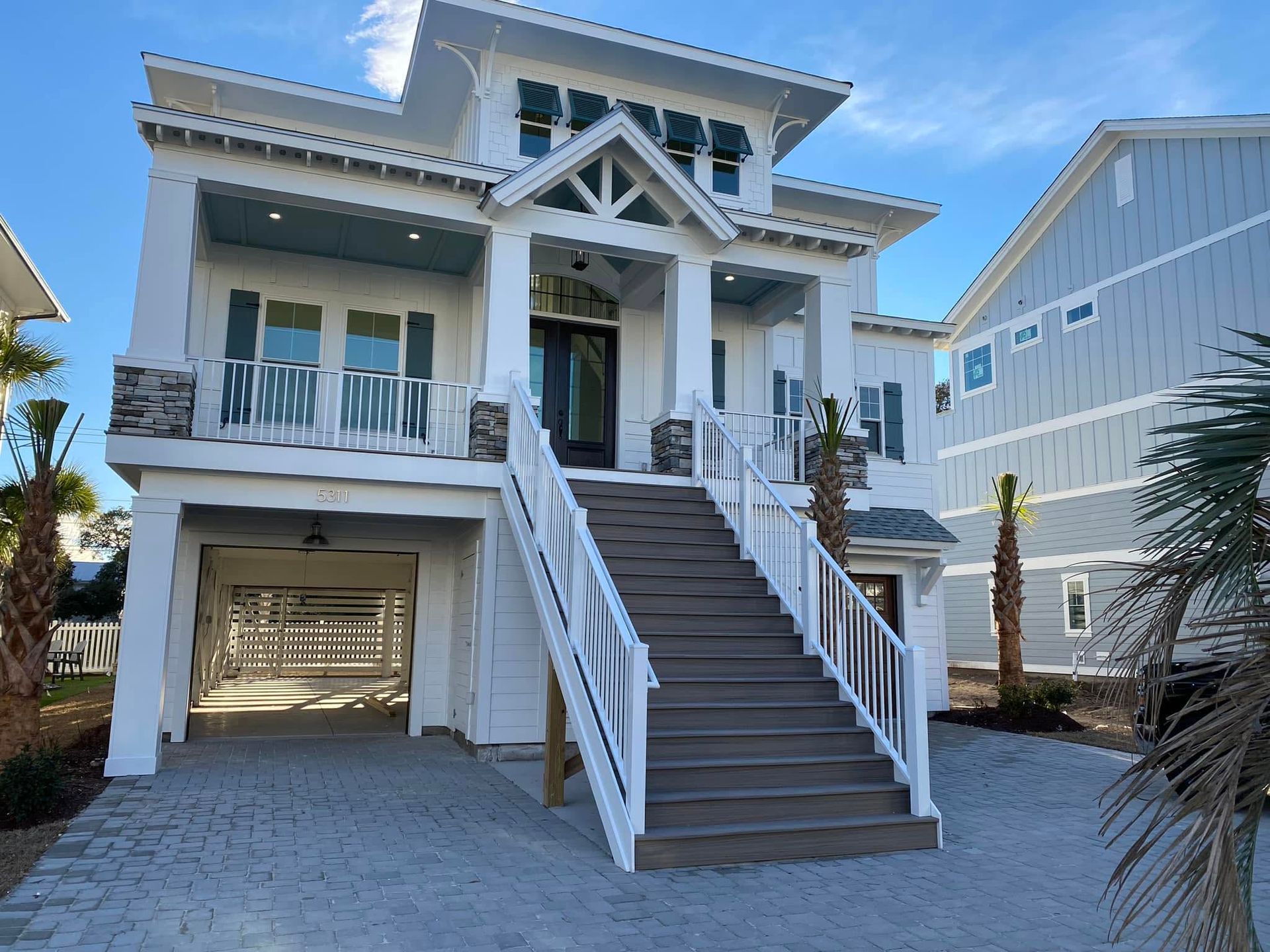 White beach house with a central staircase leading to the front entrance and a garage underneath
