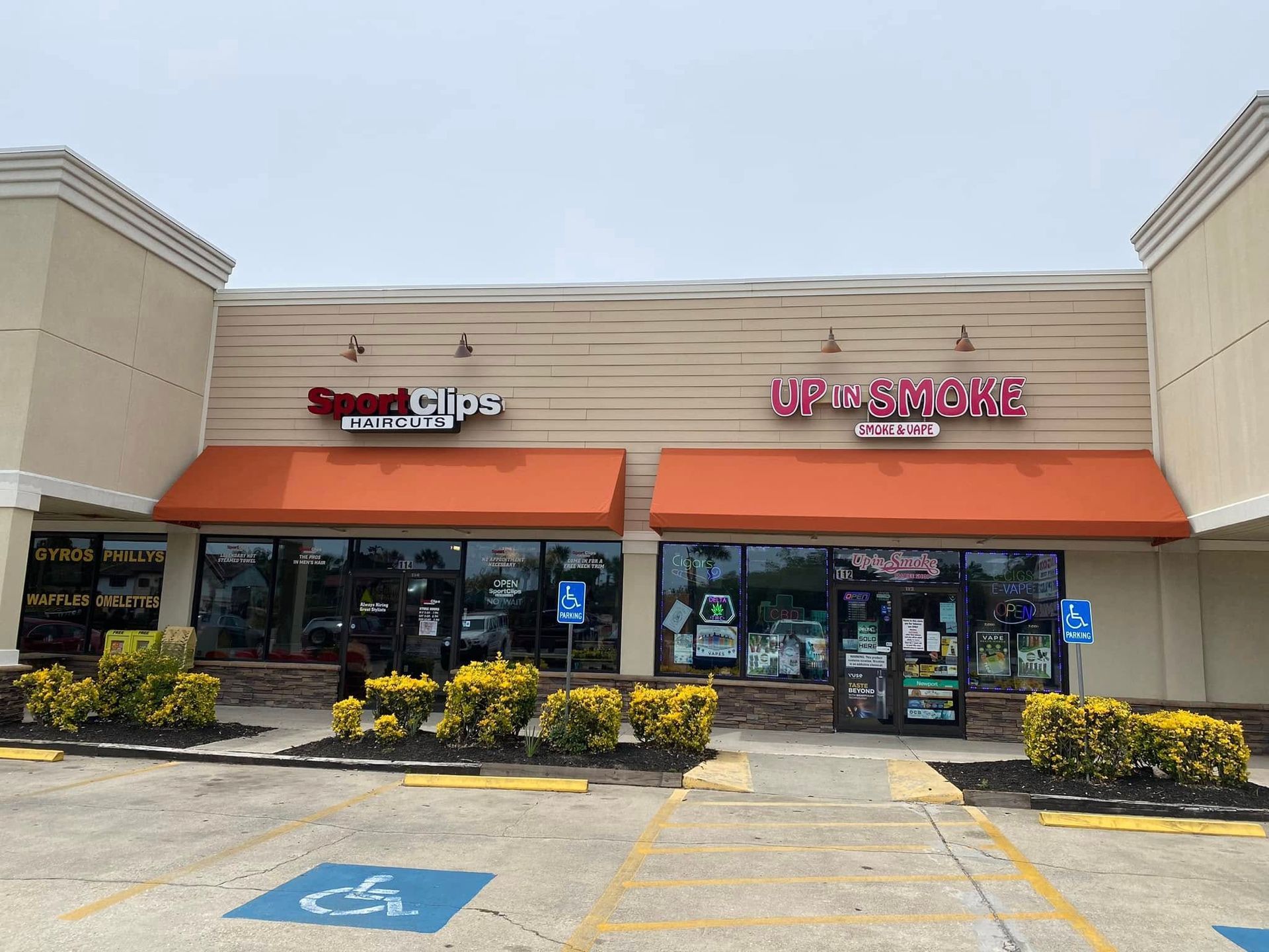 Strip mall storefronts with orange awnings and parking spaces in front.