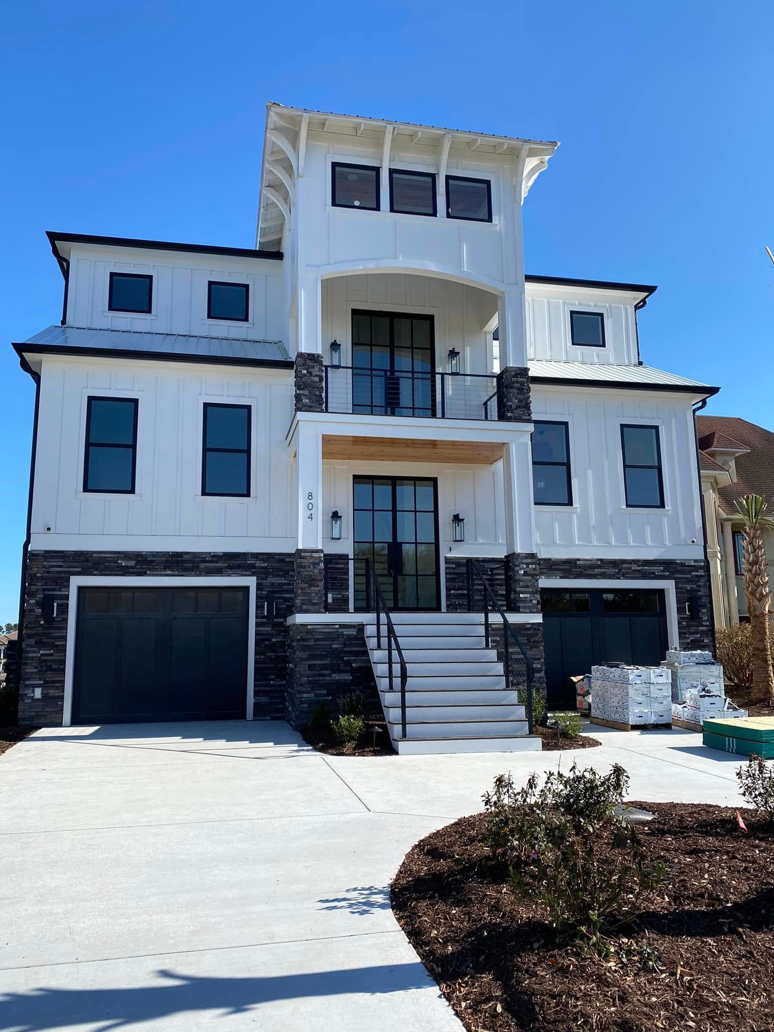 Modern white three-story house with black accents, garage, and front steps under a clear blue sky