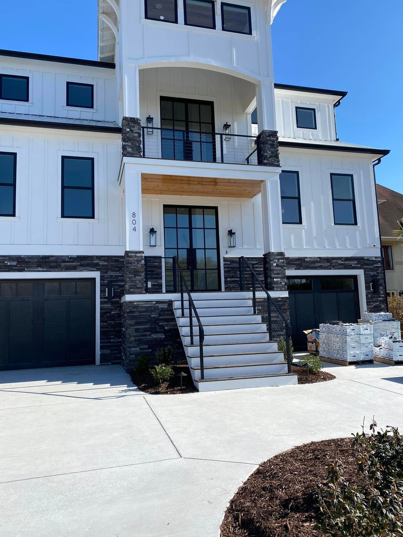 Modern white multi-story house with black garage doors and front steps under construction
