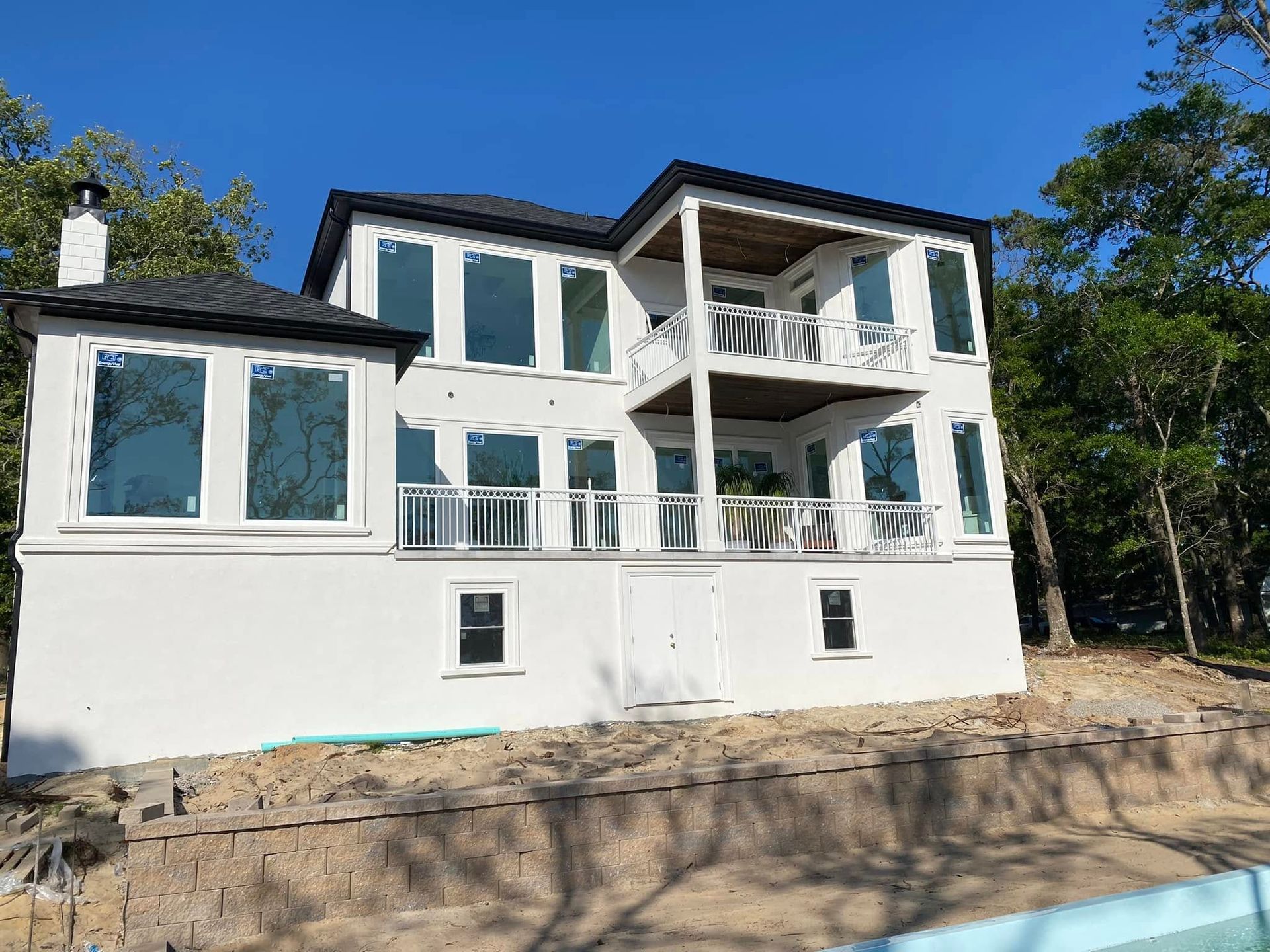 White modern house with large windows and balconies on a wooded hillside under a blue sky