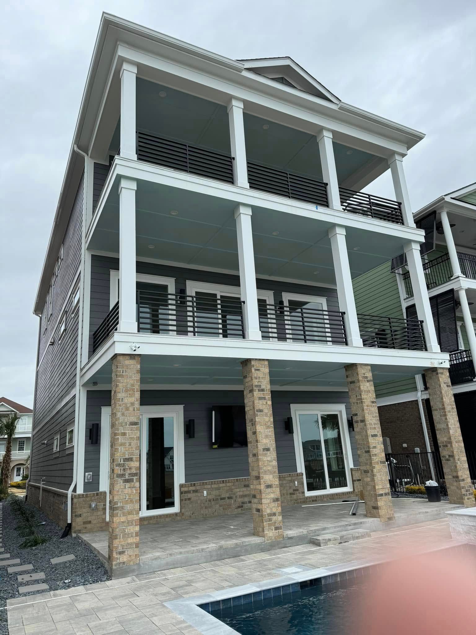 Three-story coastal house with white balconies, stone columns, and a pool in front