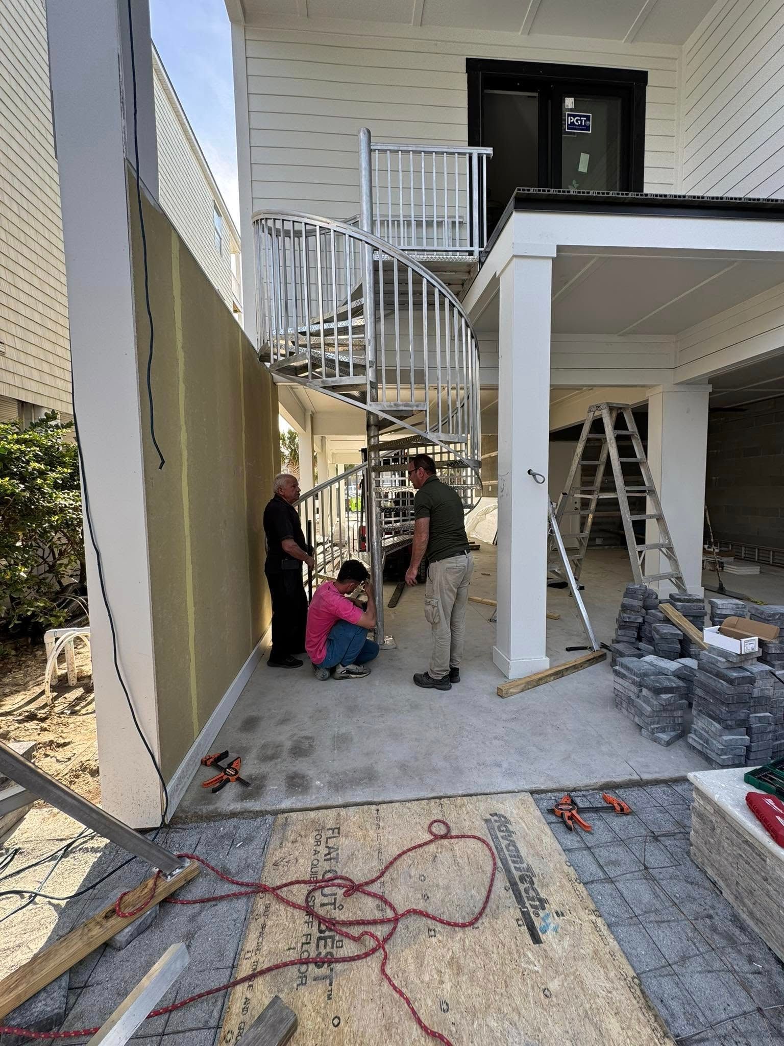 Workers installing stairs and railings beside a white house under construction.