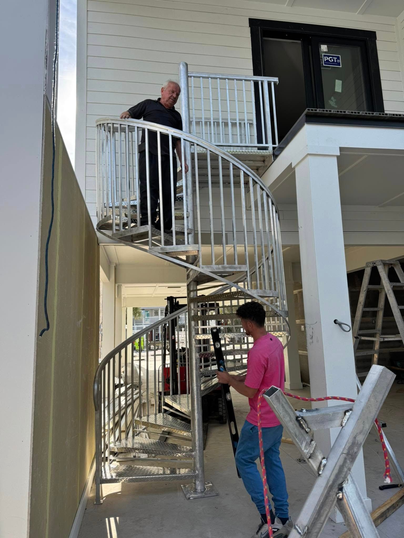 Two people on a curved outdoor staircase beside a house, with one holding a ladder at the bottom.