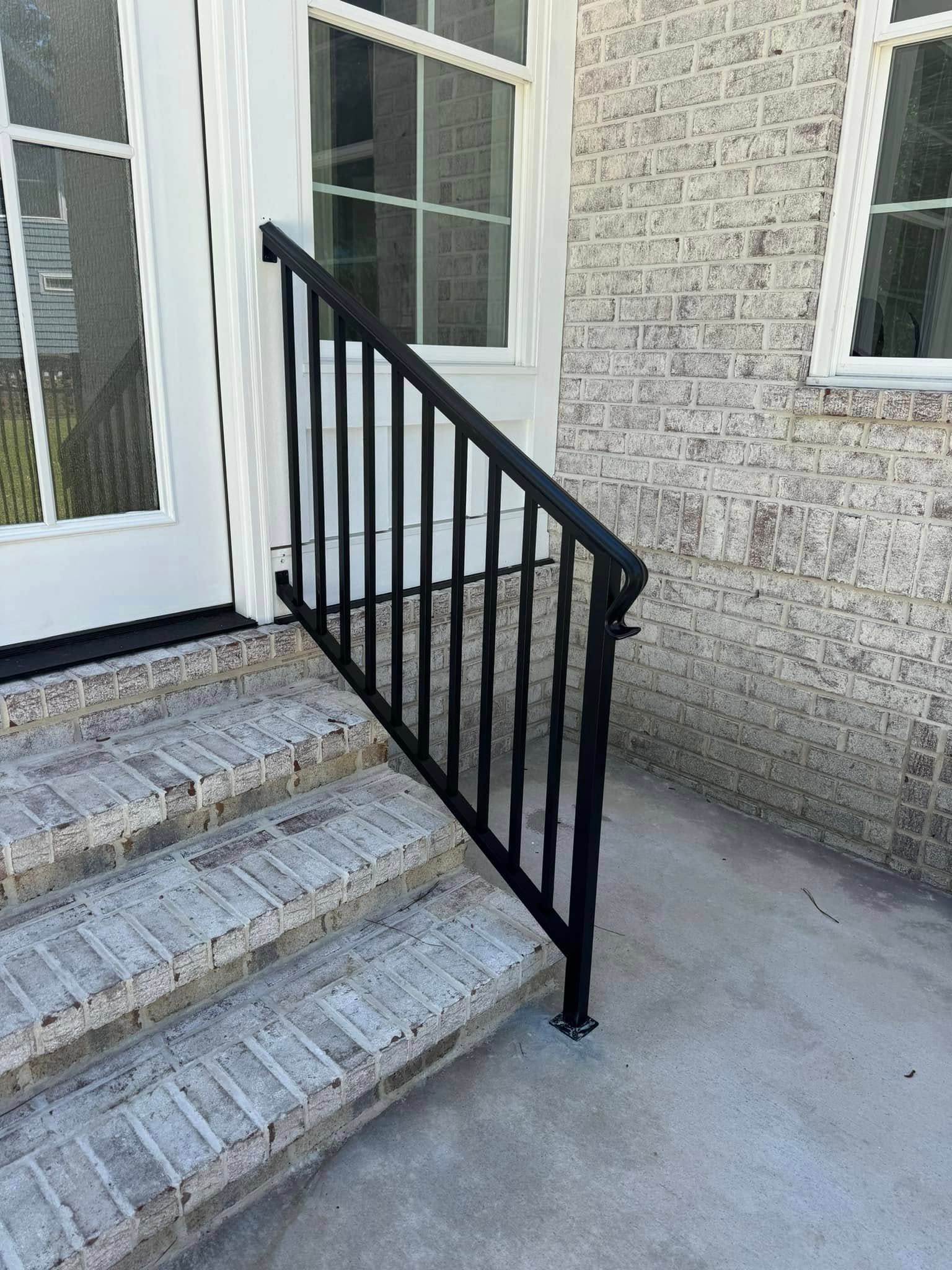 Front steps with a black metal handrail beside white doors and a textured stone wall