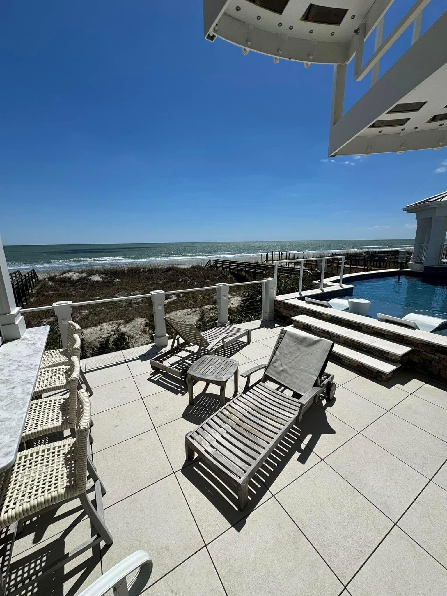 Oceanfront patio with lounge chairs, pool, and blue sky overlooking the sea