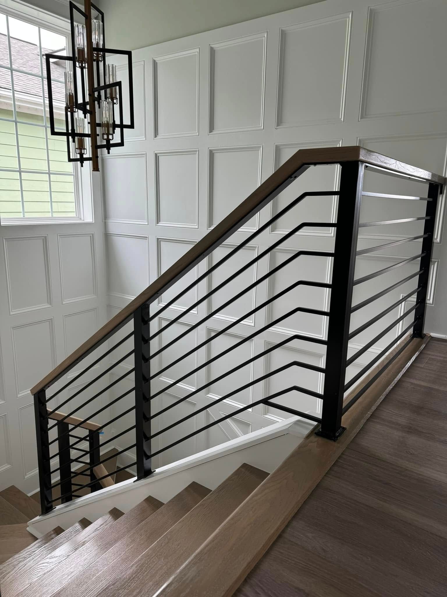 Staircase with dark metal railing in a bright interior hall with white paneled walls.