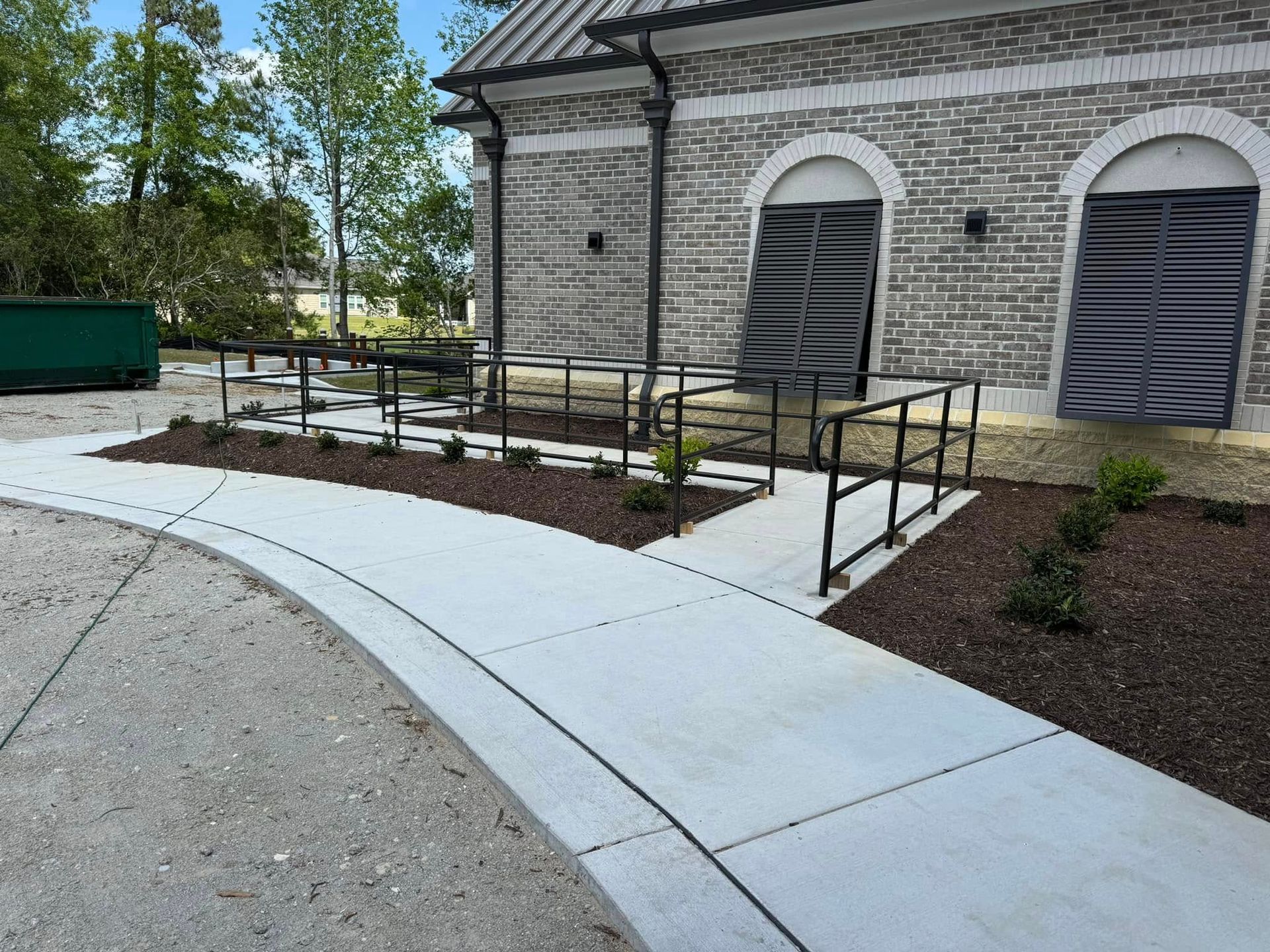Accessible curved concrete walkway with handrails leading to a brick building entrance