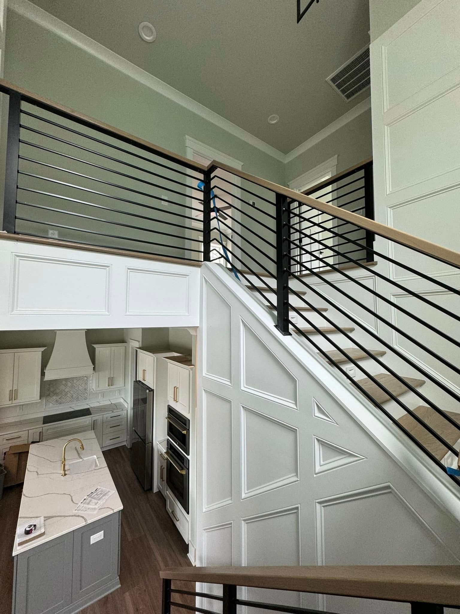 Loft view of a modern kitchen with white cabinets, wood floor, and black metal staircase railing